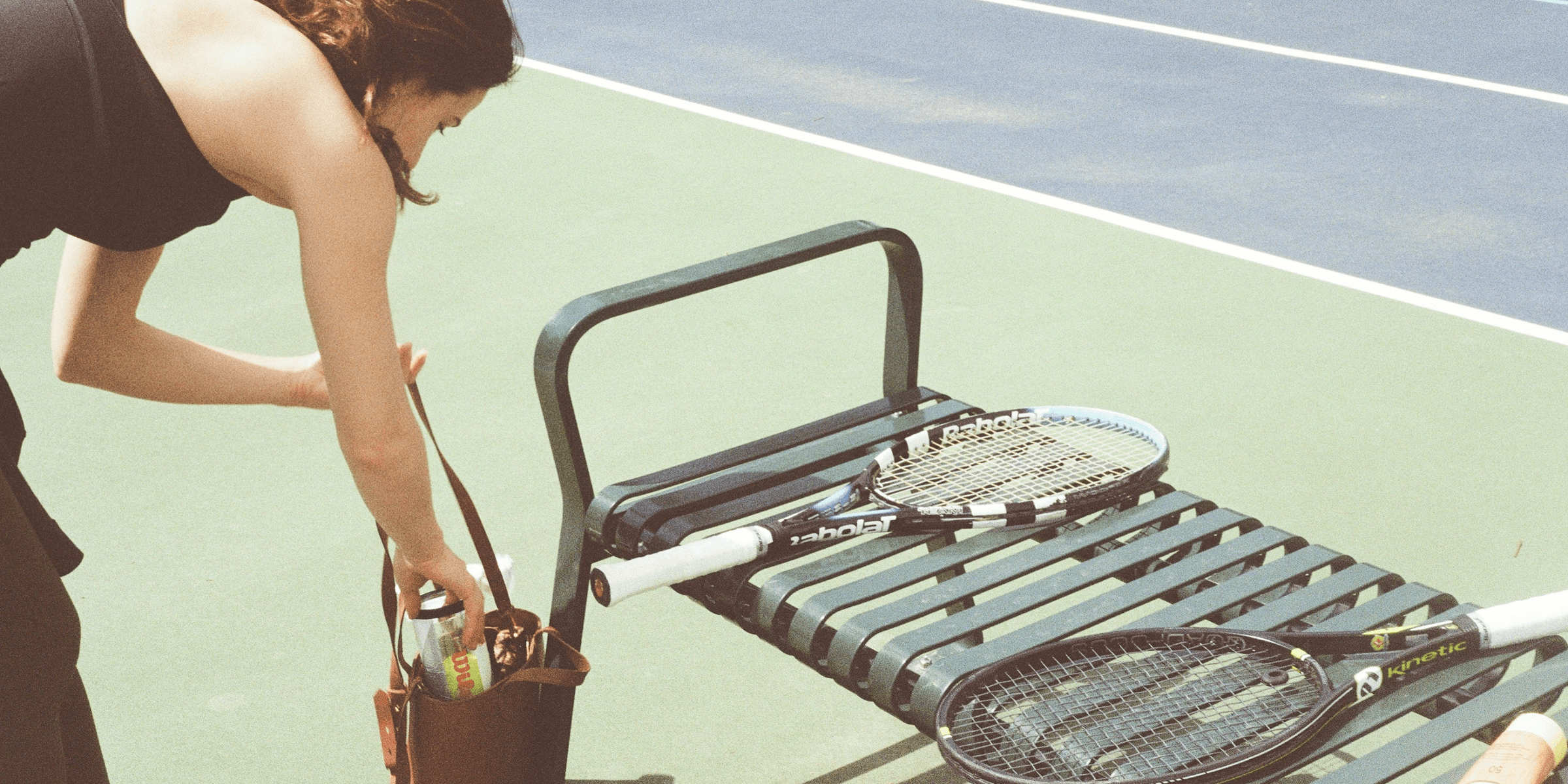 A woman bending over to pick up a tennis racket