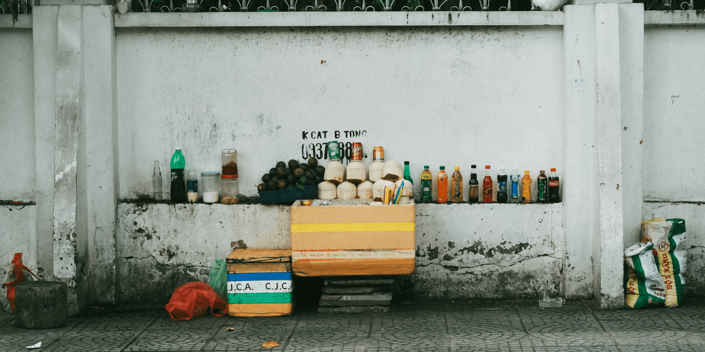 assorted-labeled bottle display on white concrete wall near gray pavement at daytime