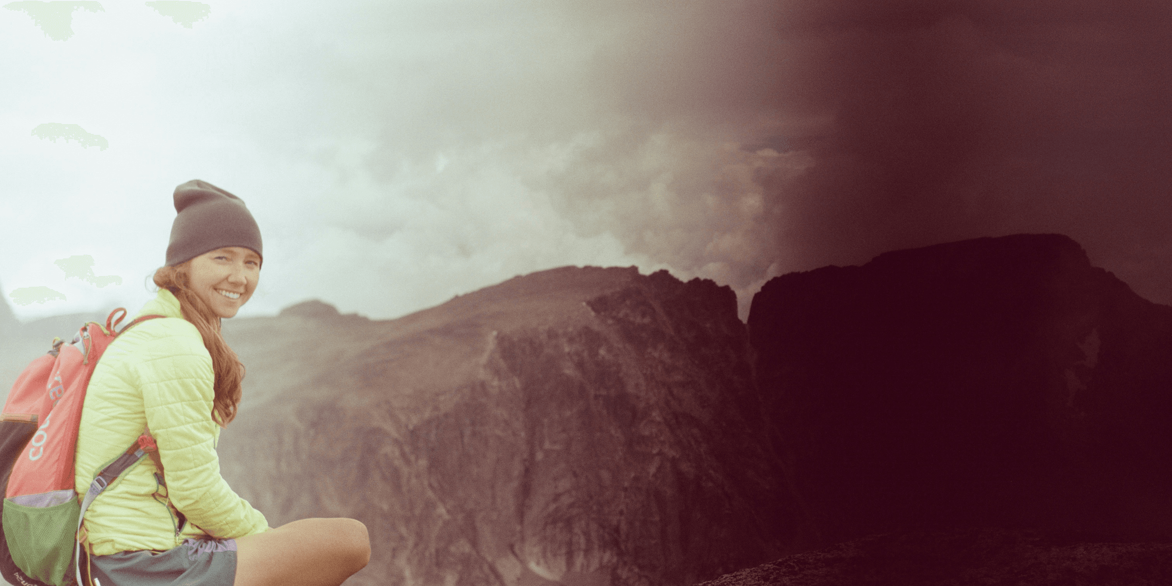 A woman sitting on top of a mountain with a backpack.