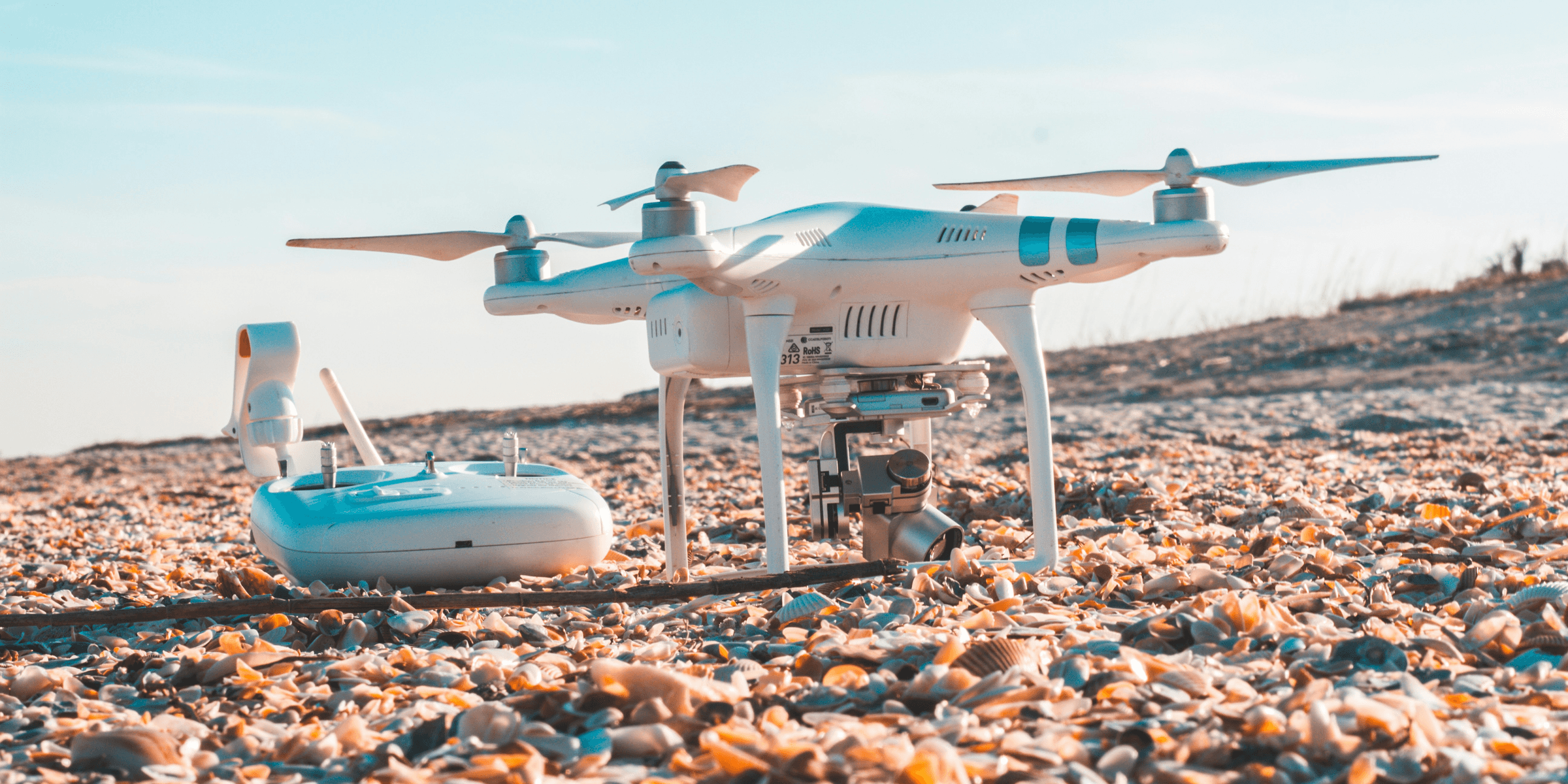 white DJI quadcopter and radio controller on rocky land.