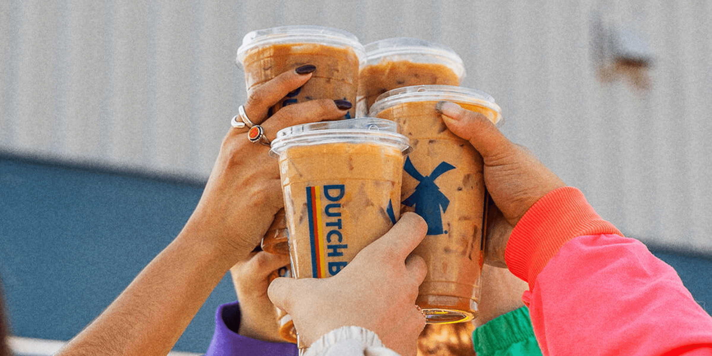 Hands holding up 4 cups of iced coffee showing the Dutch Bros logo
