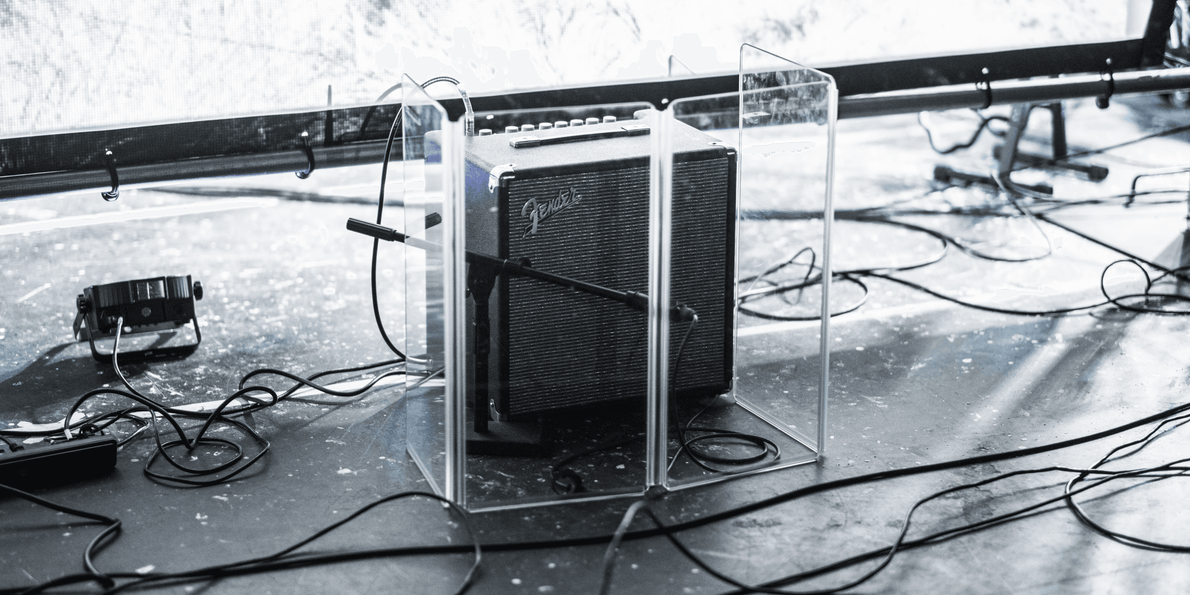 square gray and black Fender guitar amplifier enclosed by clear glass panel on top of stage beside stage lighting.