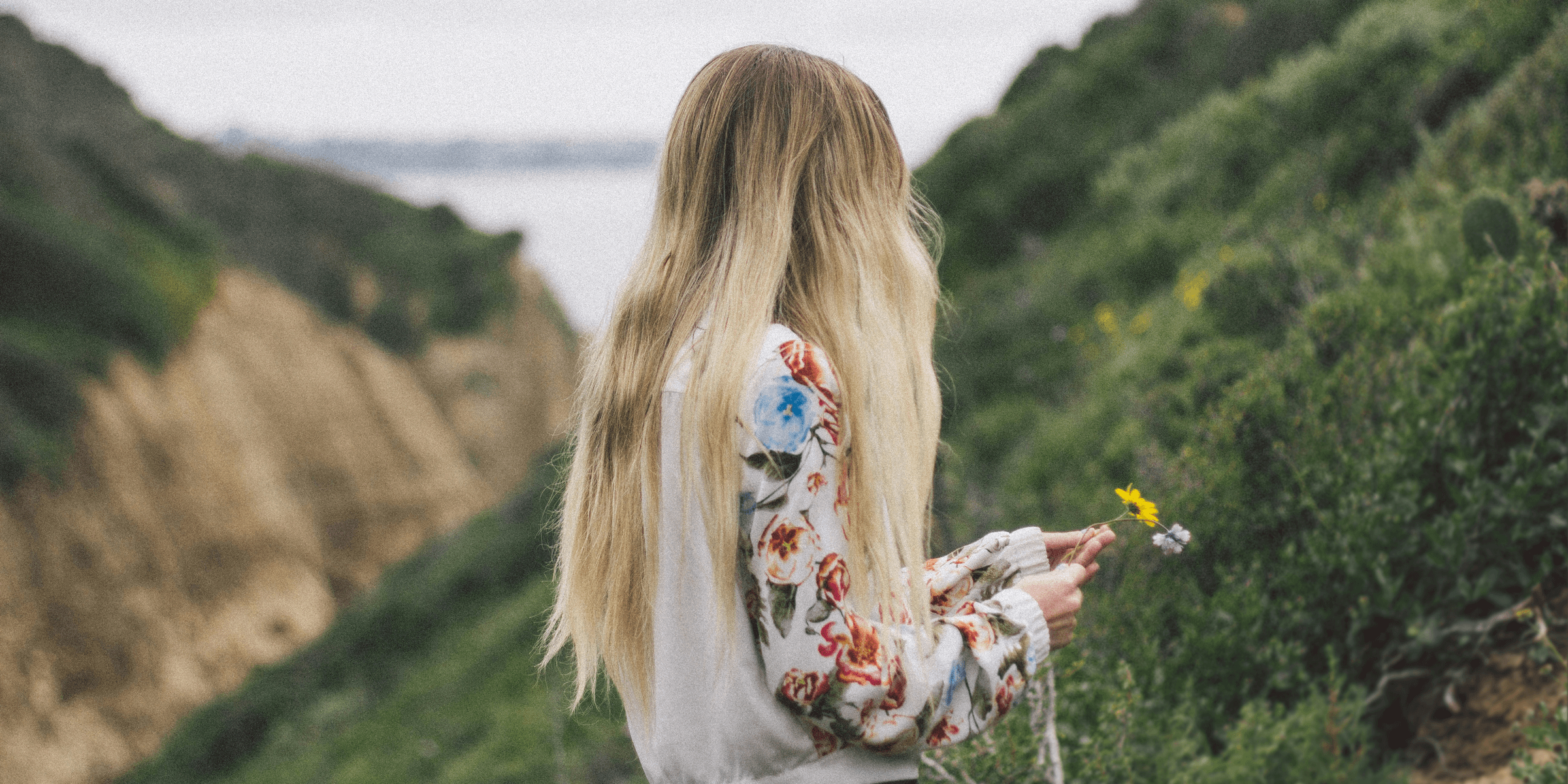 woman wearing white, green, and red floral long-sleeved shirt standing on green leaf plant covered hillside during daytime