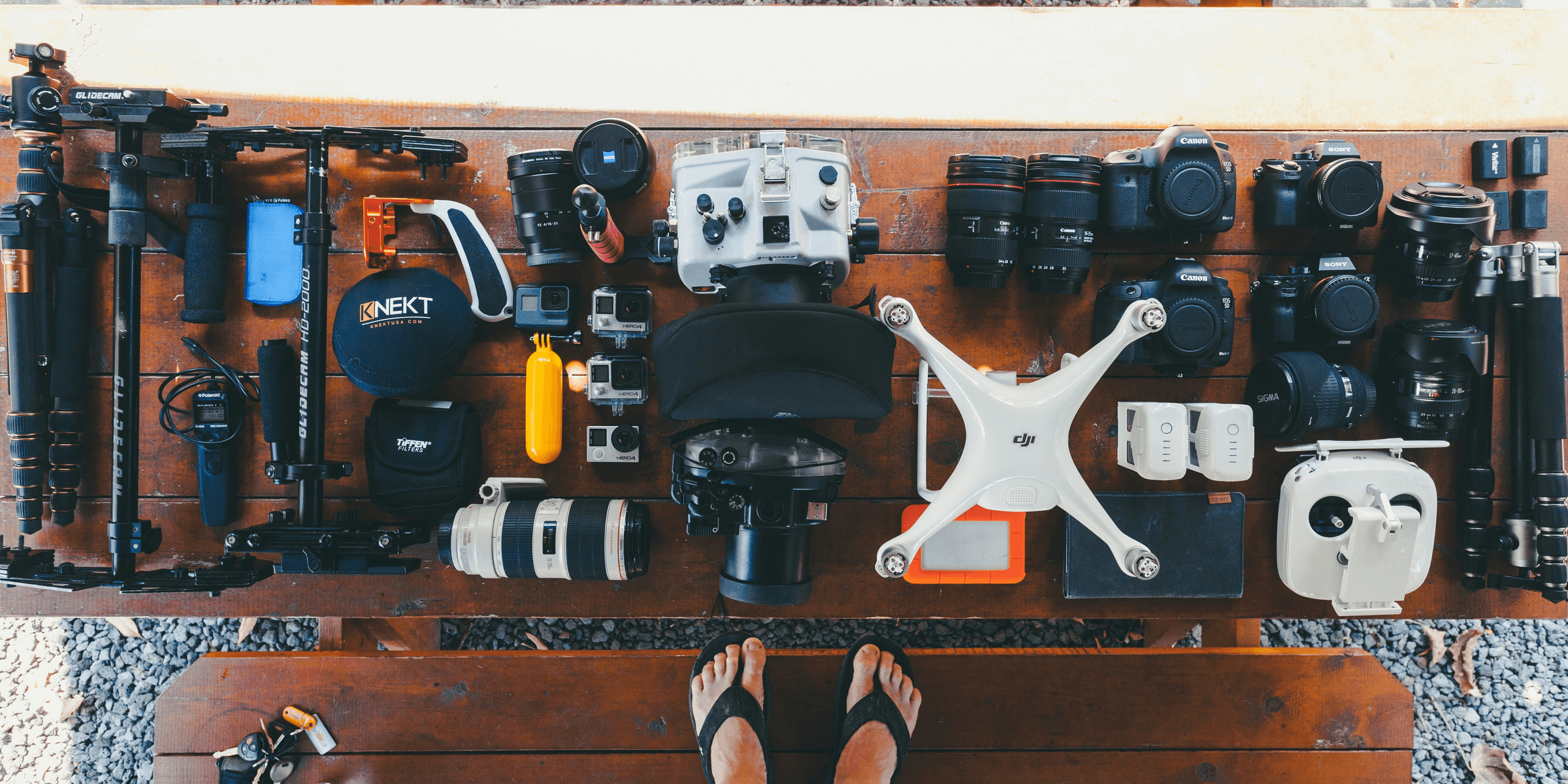 person standing near black and white quadcopter drone near cameras on brown wooden table.