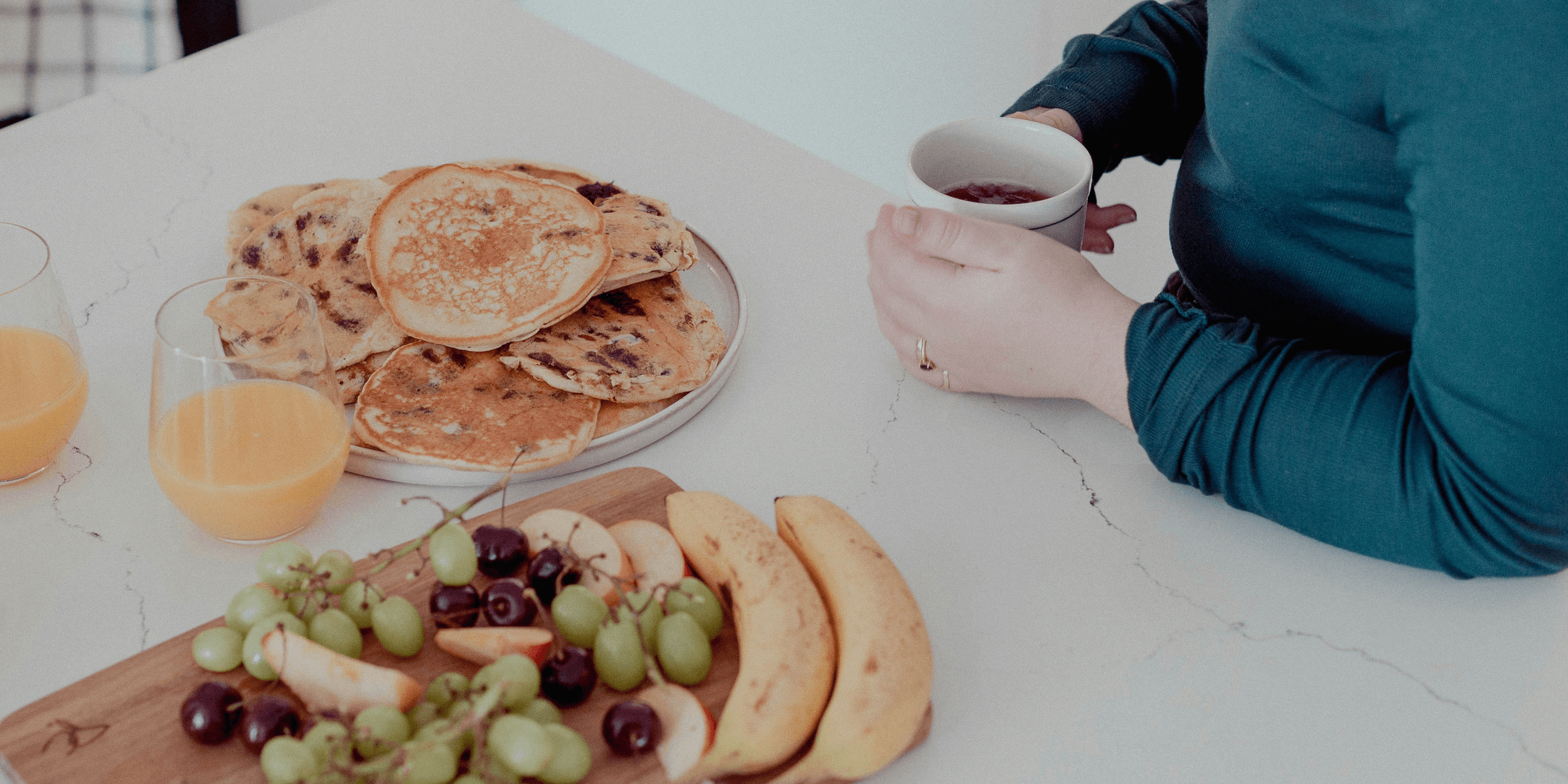 a woman sitting at a table with a plate of fruit and pancakes.