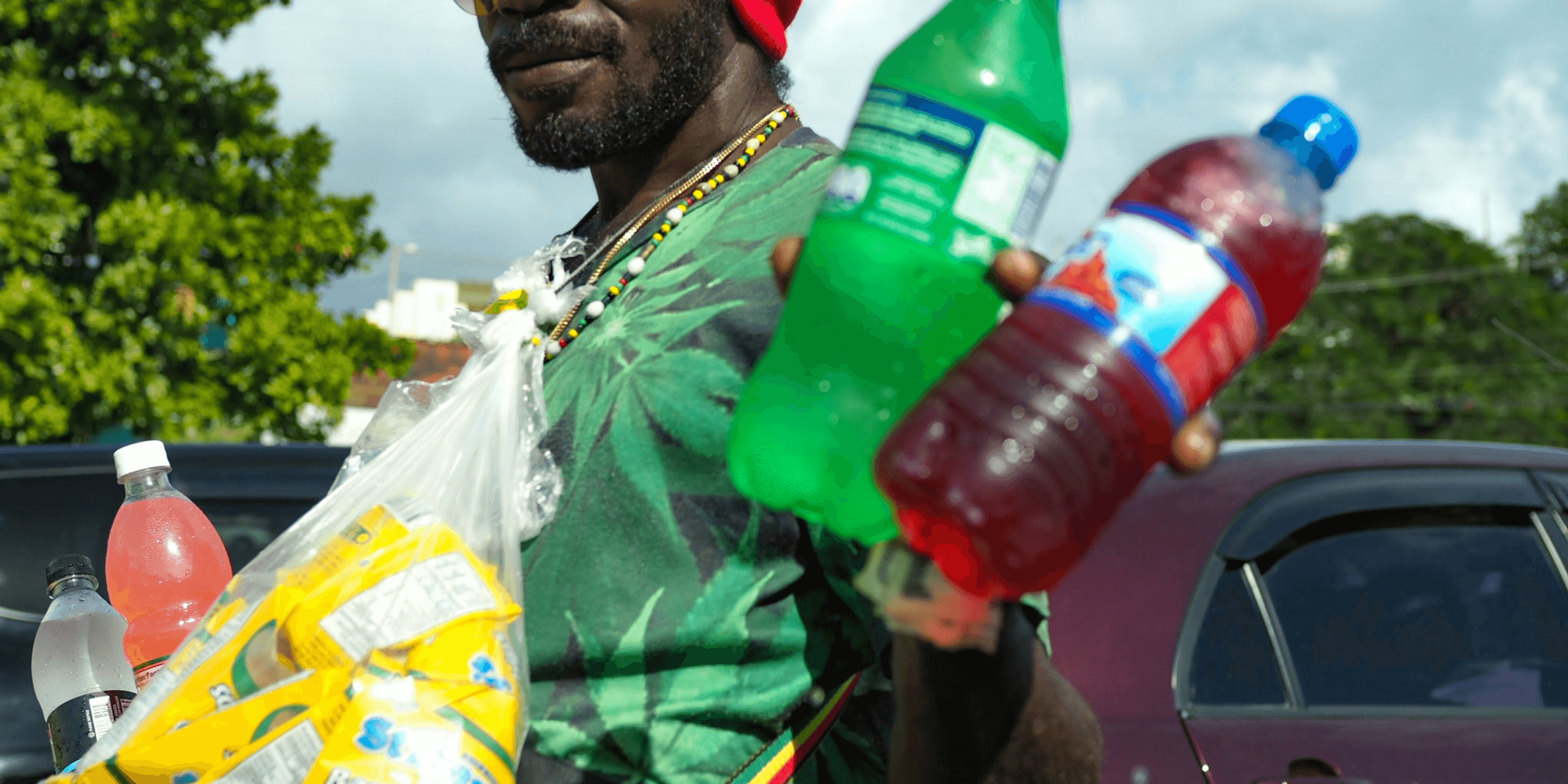 man wearing green t-shirt holding two Sprite and blue labeled bottles.