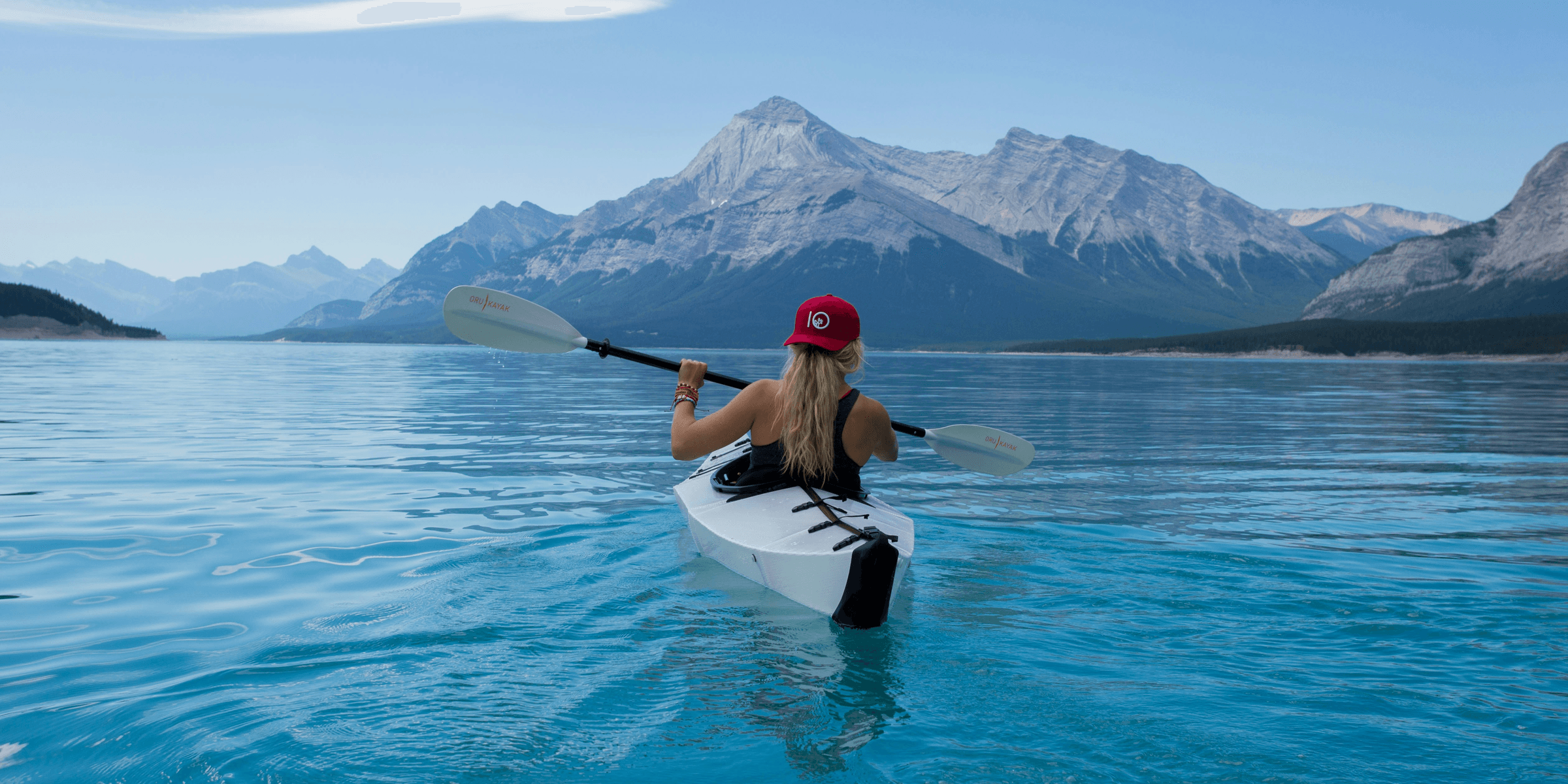 woman wearing red hat riding on white kayak facing mountain alps.