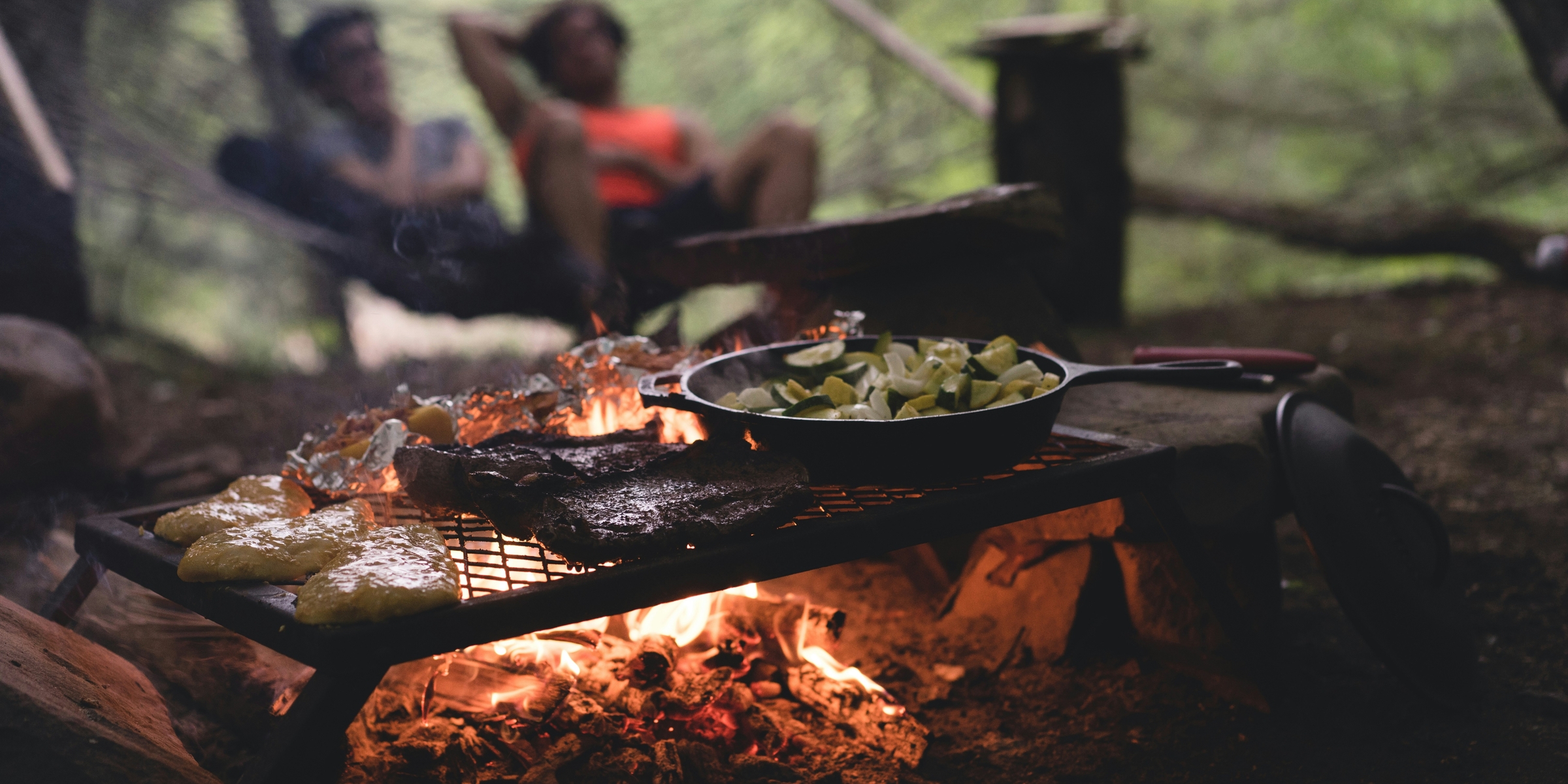 selective focus photo of skillet and meat on top of grill with fire.