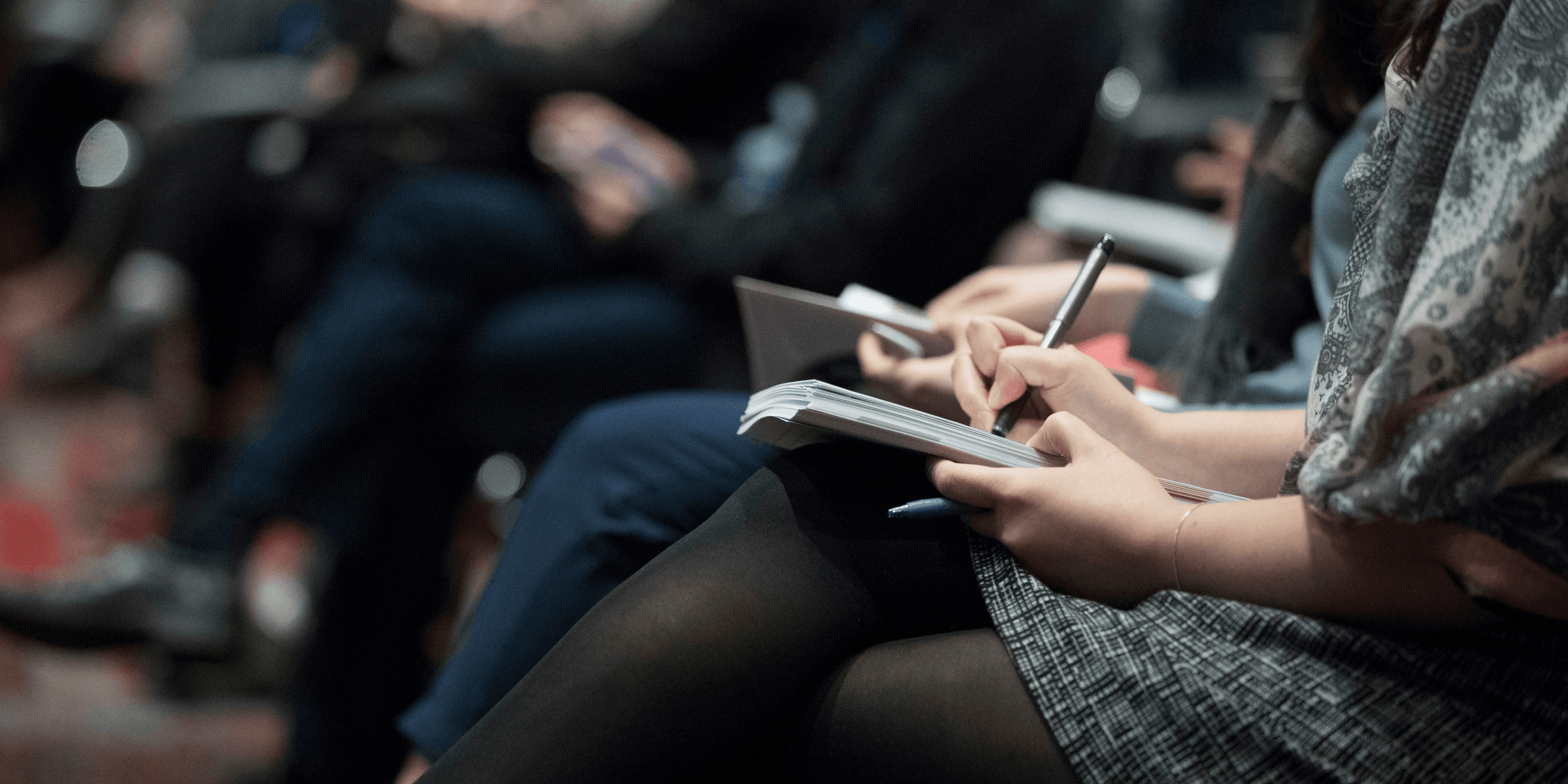 selective focus photography of people sitting on chairs while writing on notebooks.