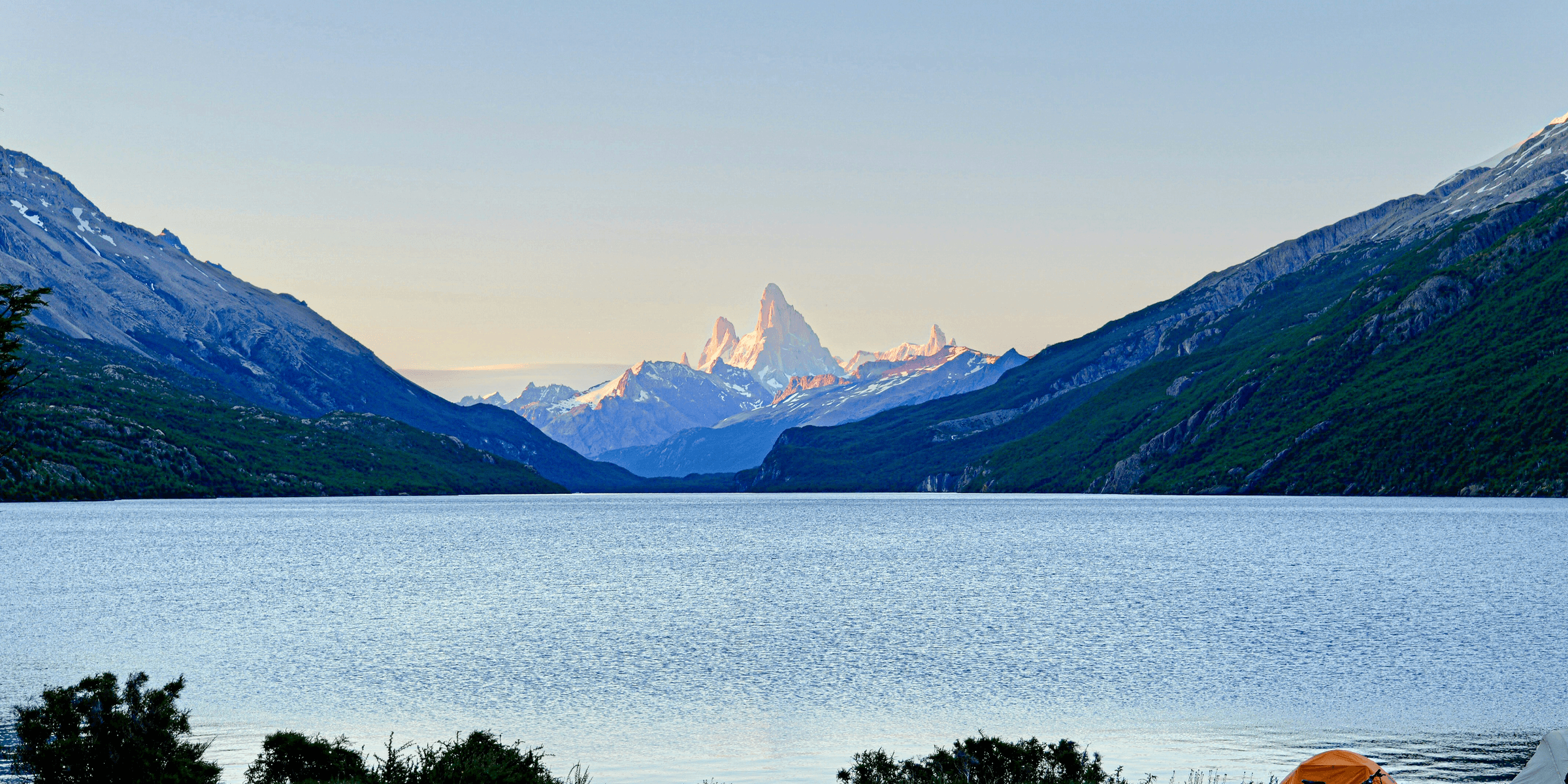 a tent is set up on the shore of a lake with mountains in the background