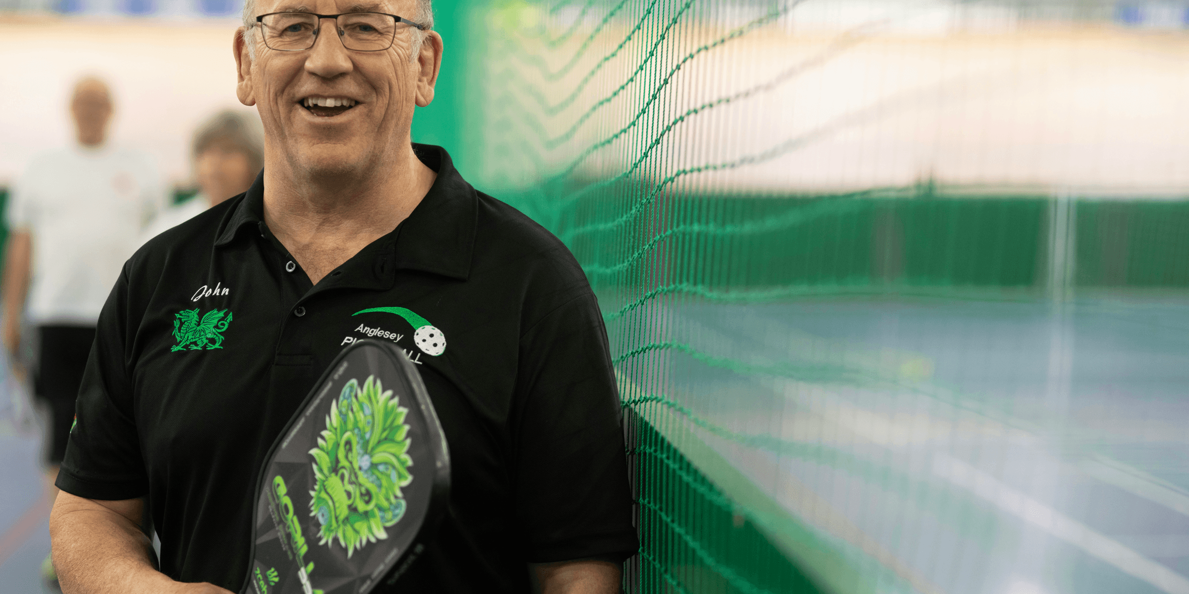 A smiling man holds a pickleball paddle..