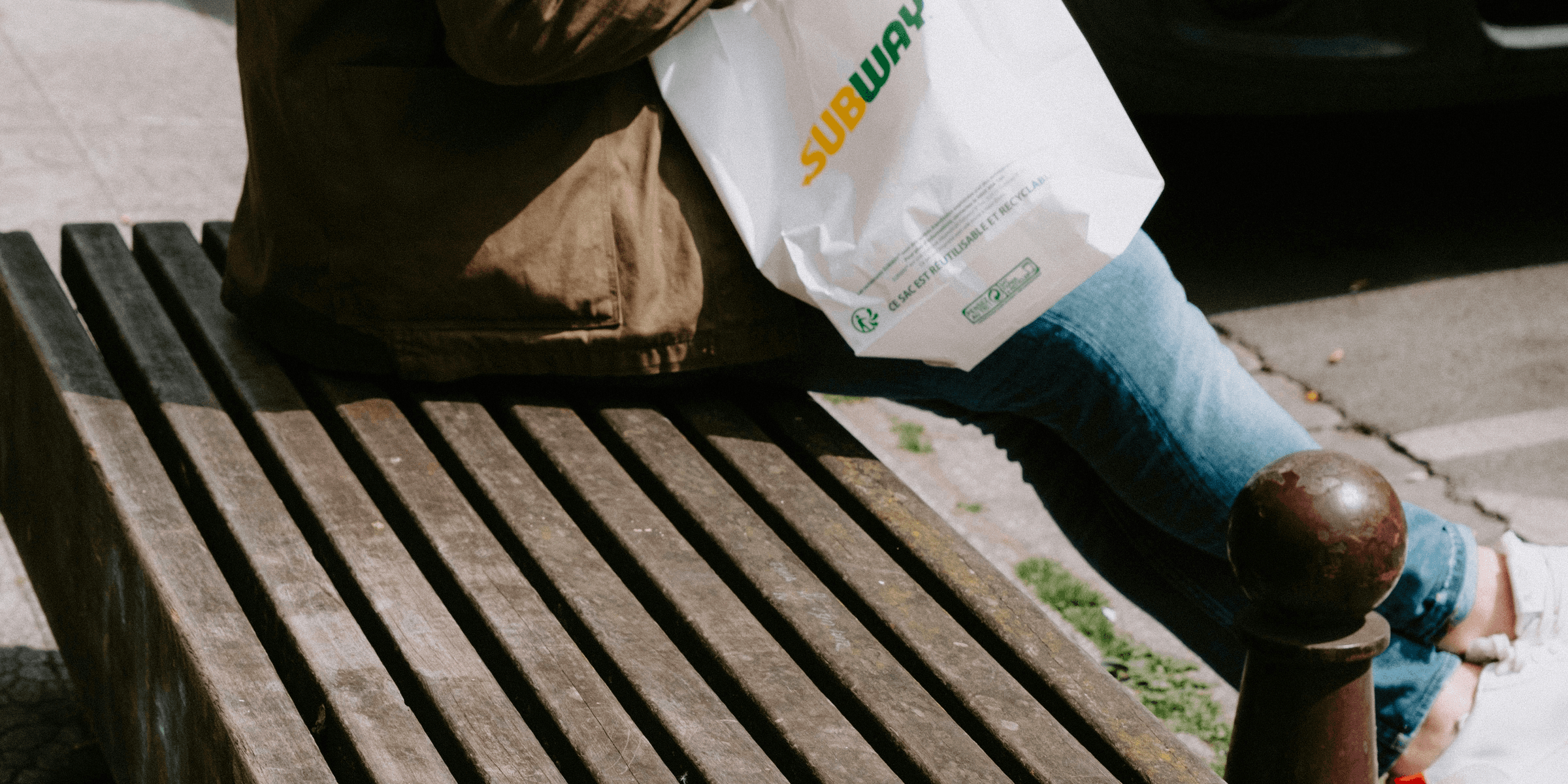 a person sitting on a bench with a bag of food.