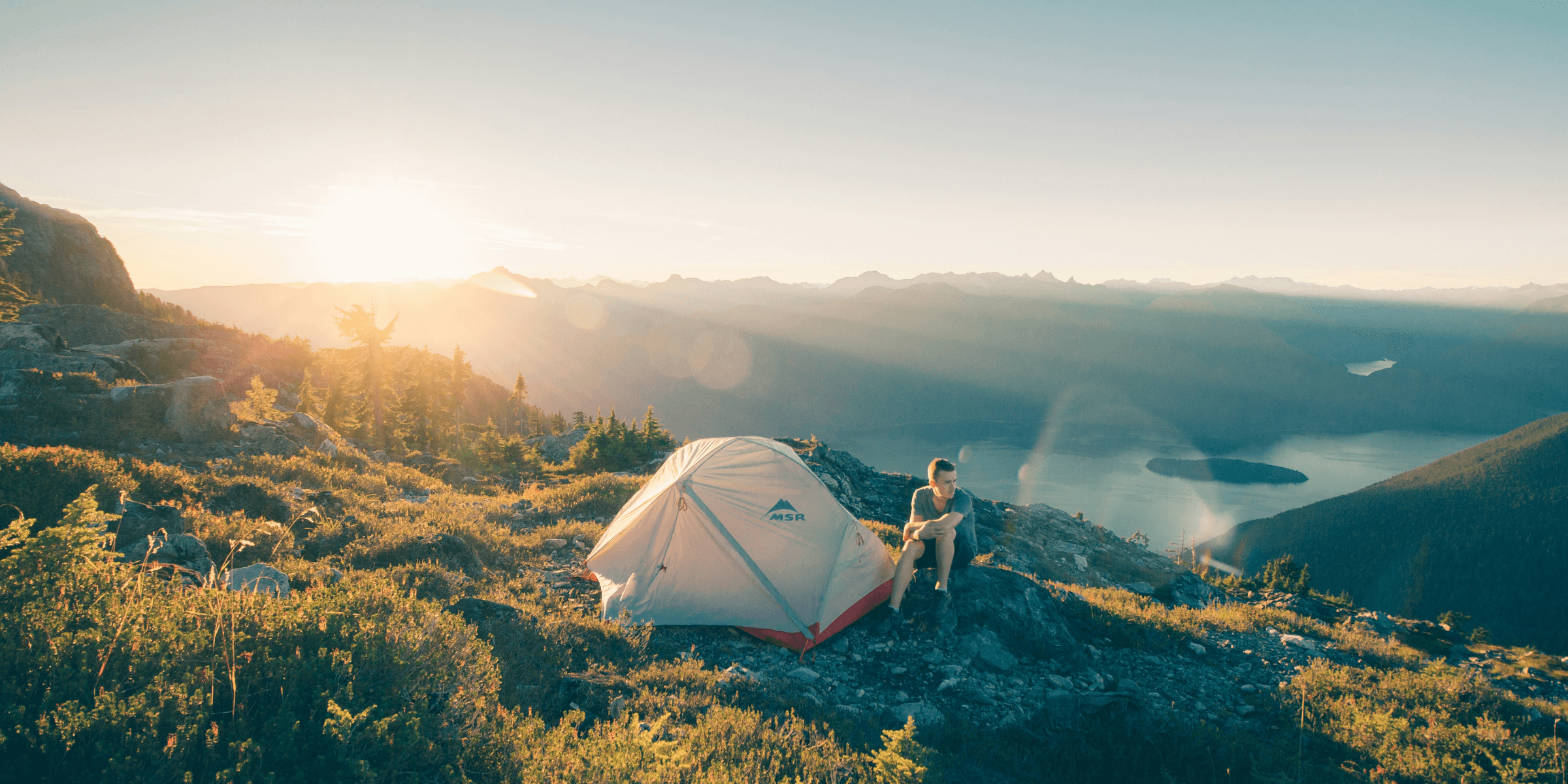 man sitting on stone beside white camping tent.