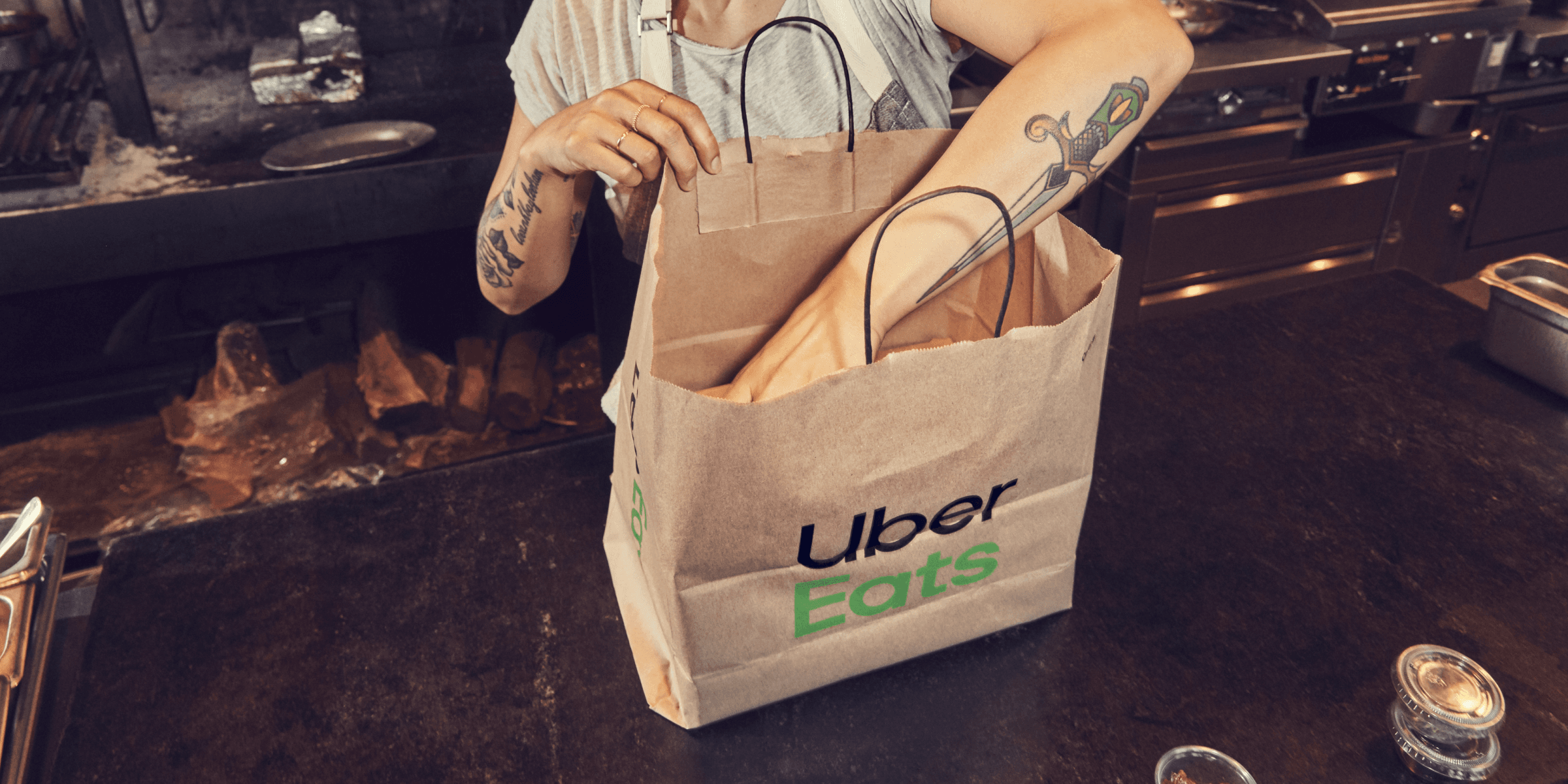 Brown bag on a table displaying the Uber Eats logo, with an arm reaching into the bag