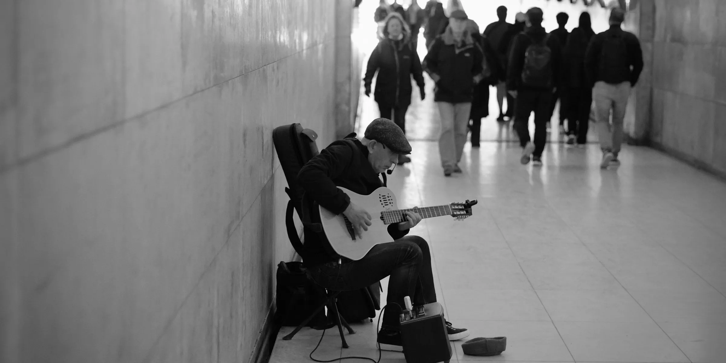 Man plays guitar in subway station while people walk by