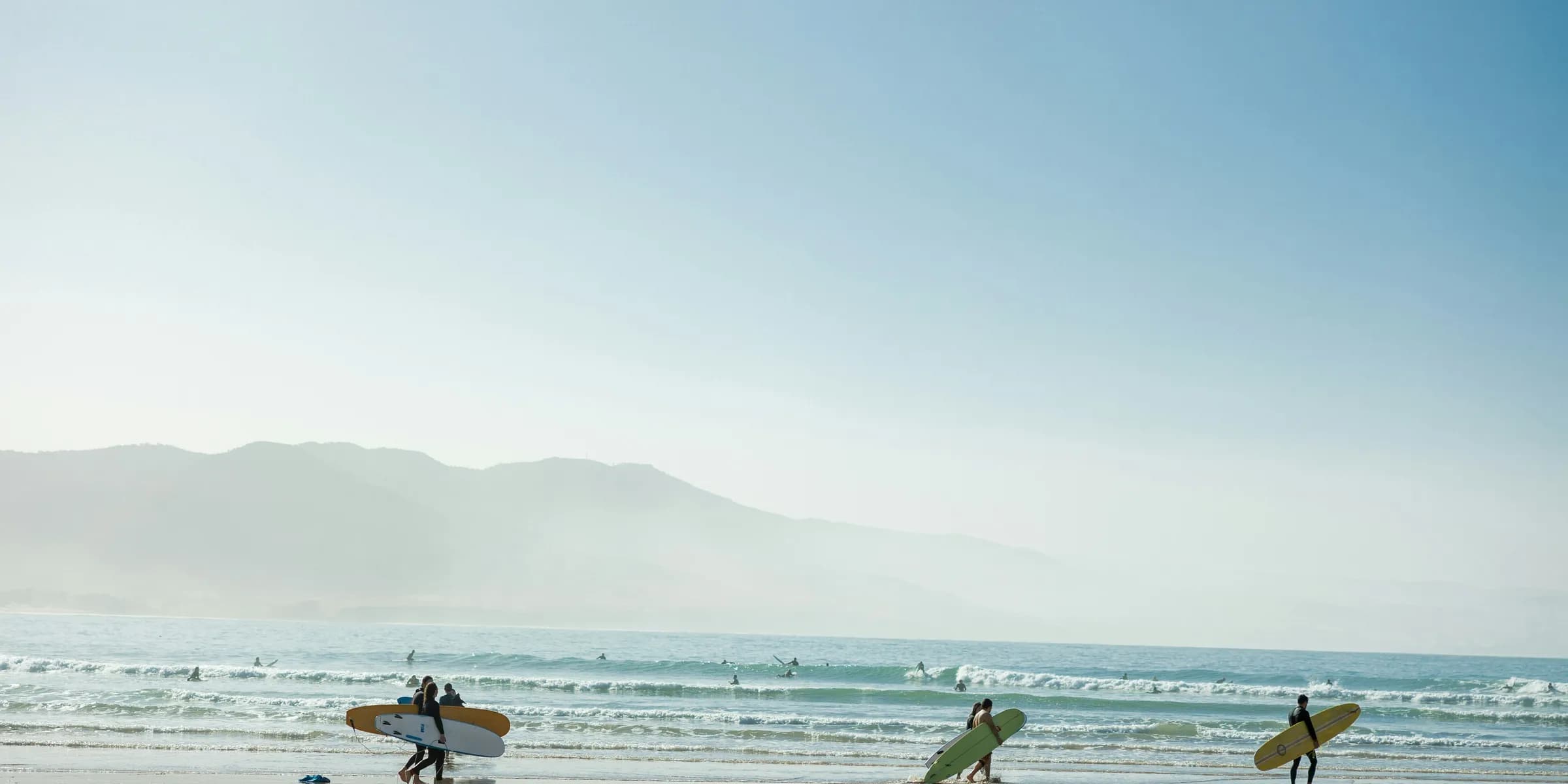 a group of people carrying surfboards on top of a beach