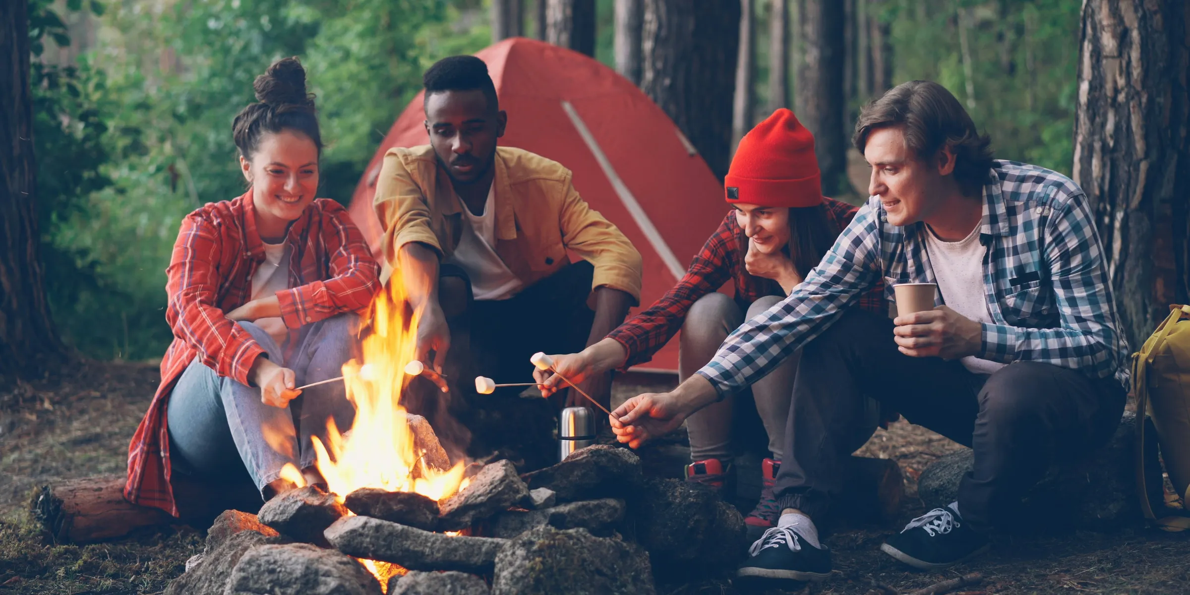 Friends roasting marshmallows around a campfire at campsite.