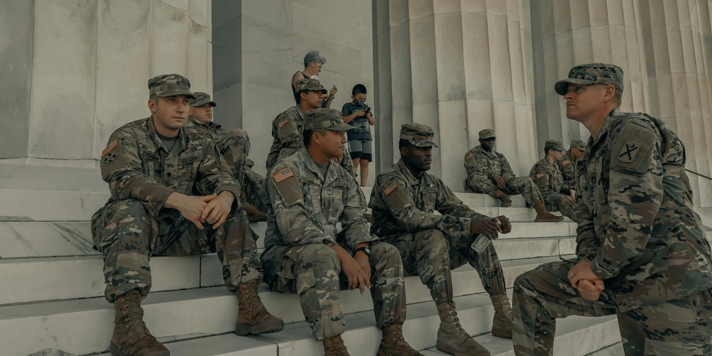 men in camouflage uniform standing near white wall