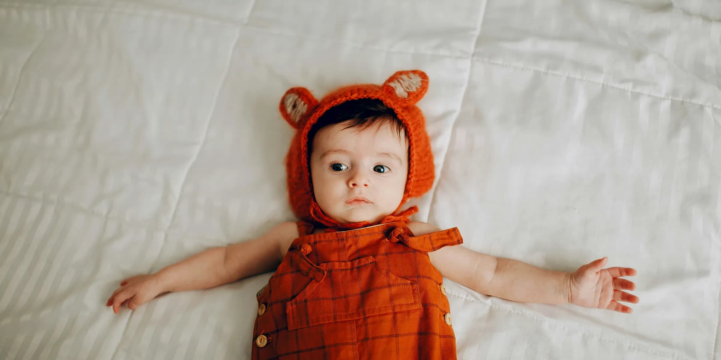 baby in red and black plaid dress lying on white bed