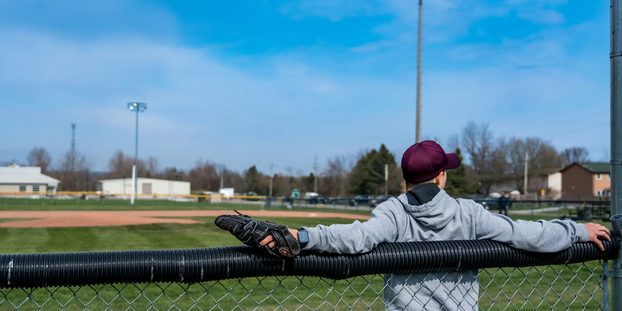 a young boy leaning on a fence at a baseball field
