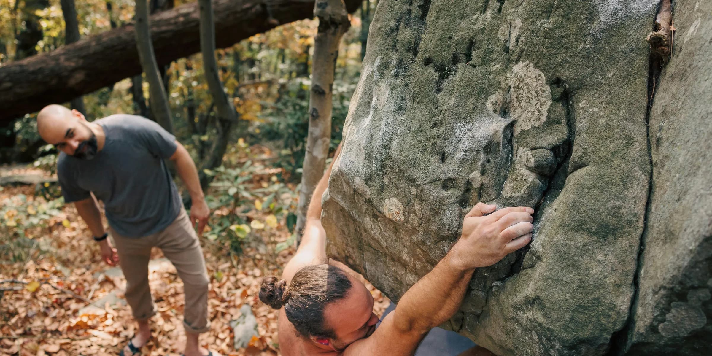 Two men climbing up a large rock in the woods