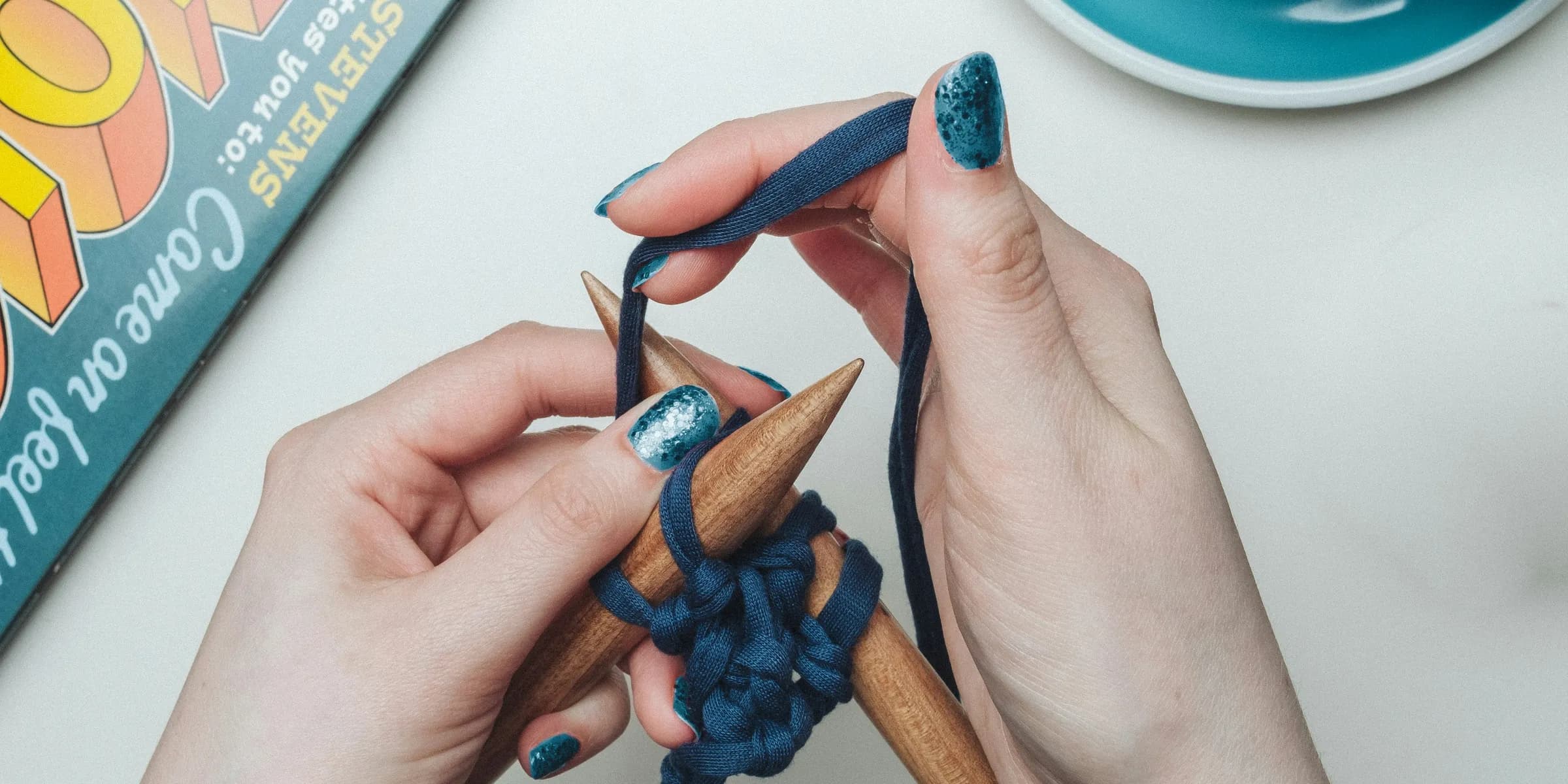 person tying blue lace on two brown sticks beside teal and white ceramic teacup set