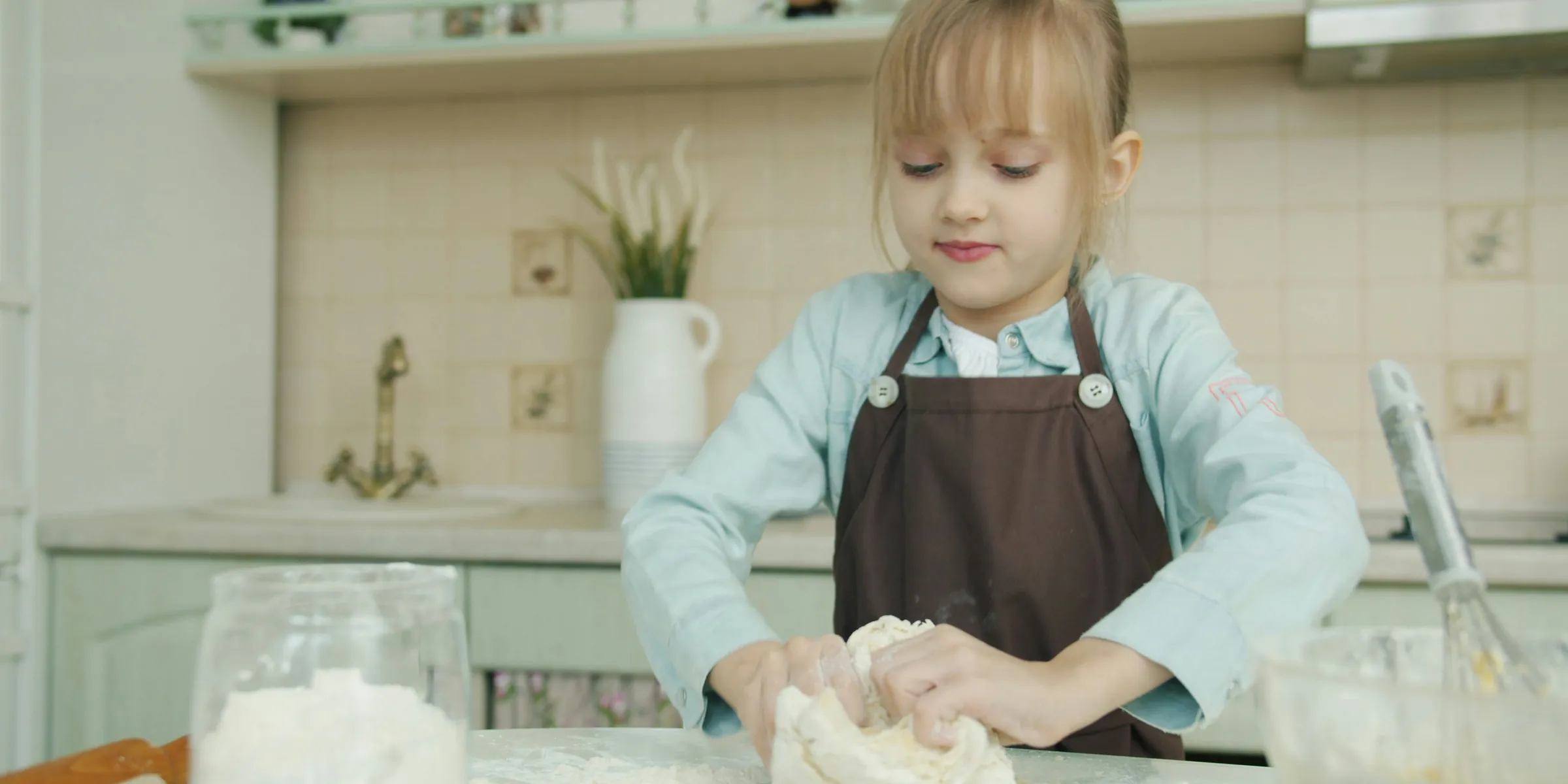 Young girl kneading dough in a kitchen.