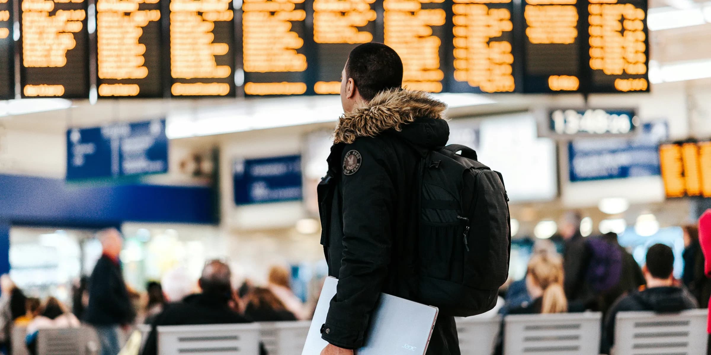 man standing inside airport looking at LED flight schedule bulletin board