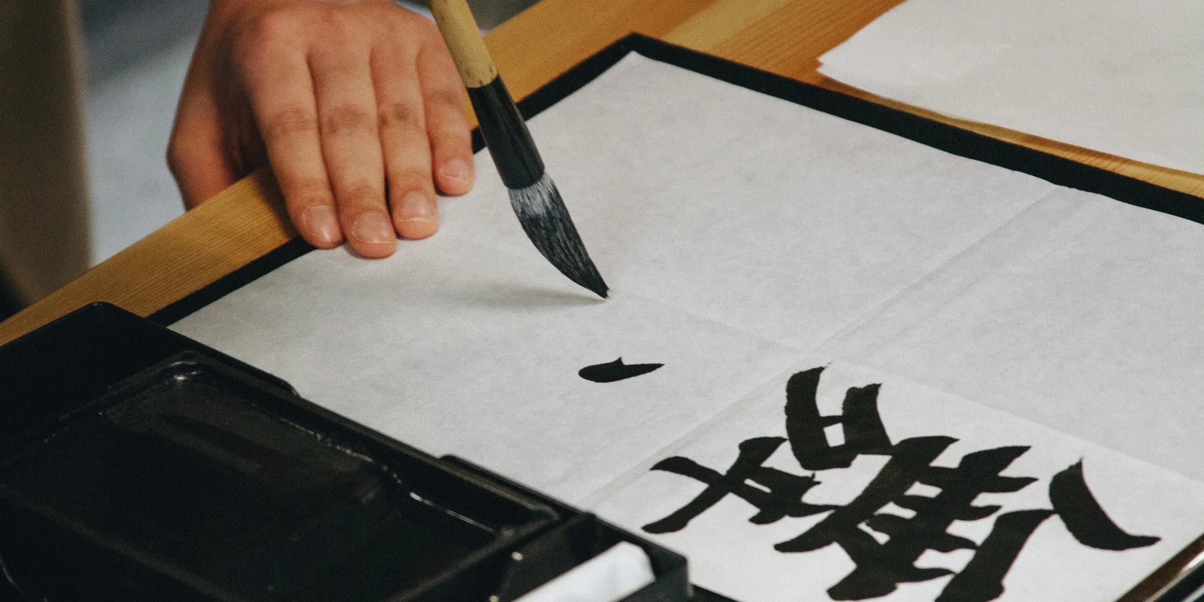 person holding black paint brush while painting black text on white paper
