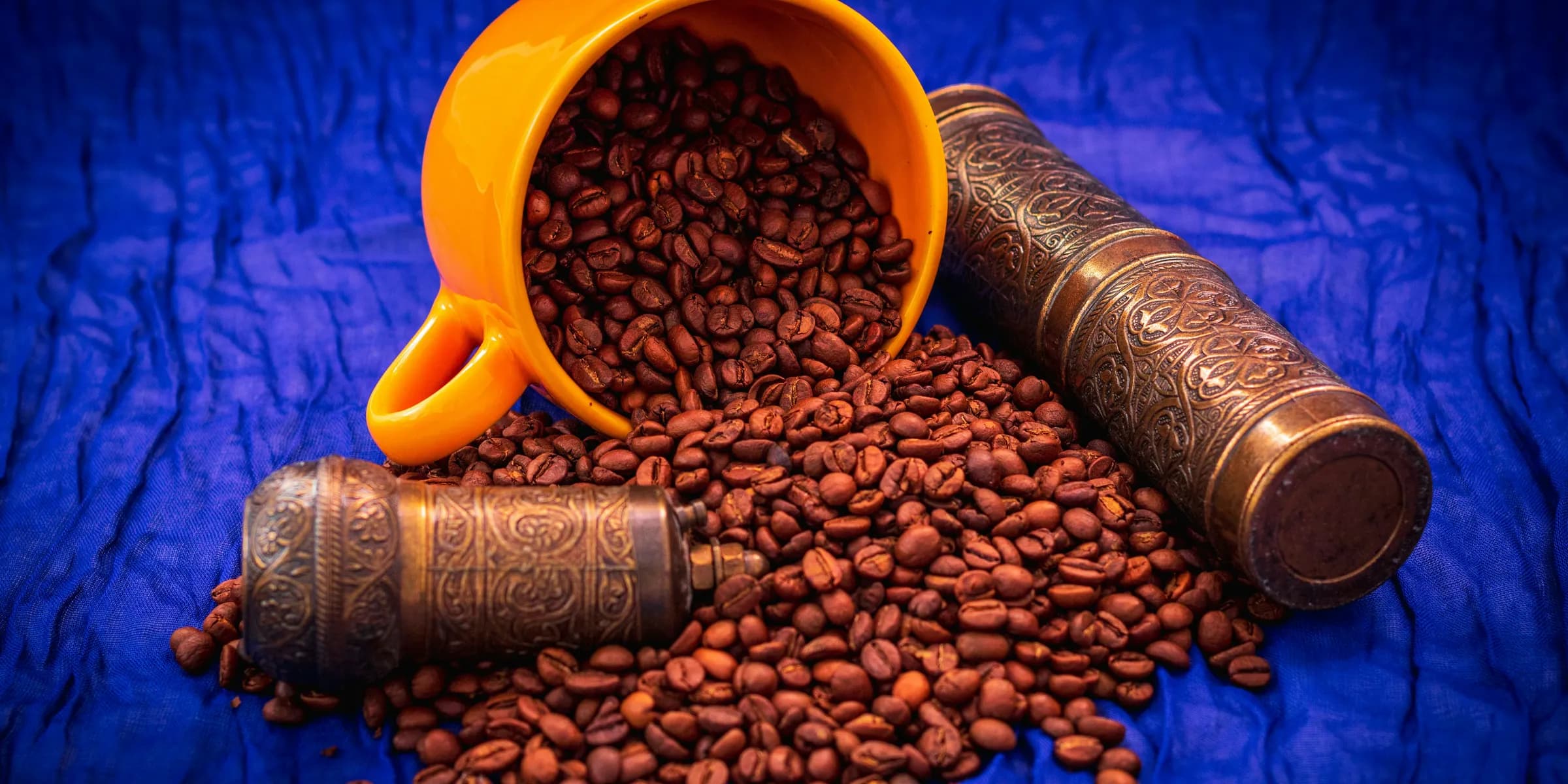 Coffee beans spill from a cup with a grinder.