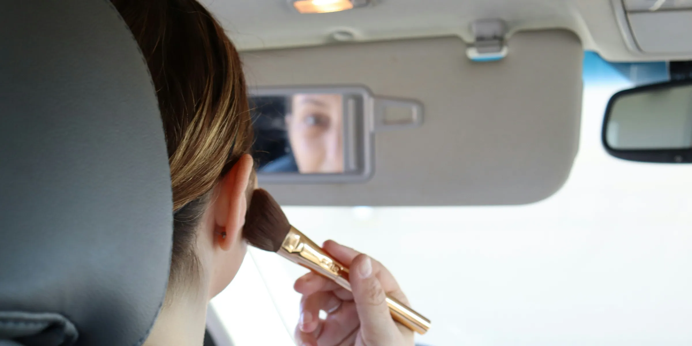 woman in gray sweater holding brown makeup brush