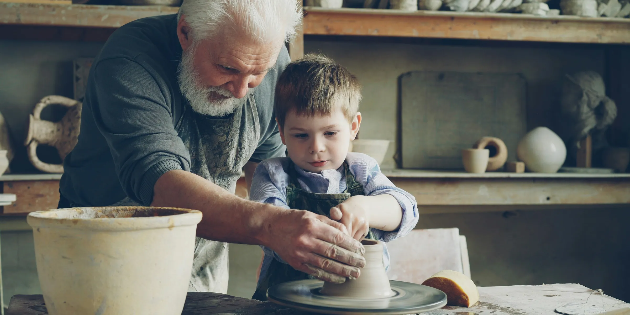 A grandfather teaches a child how to make pottery.