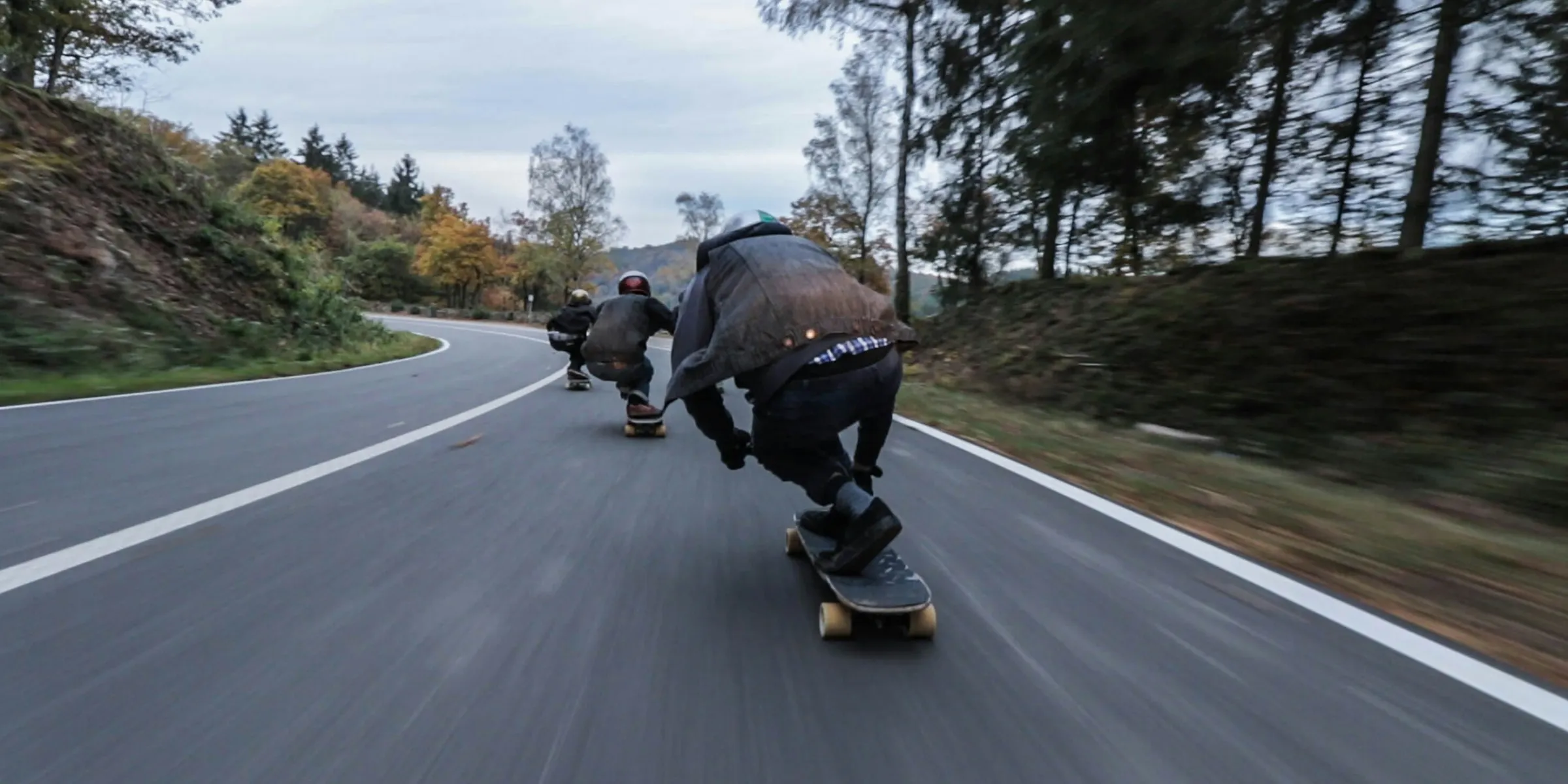 three person riding skateboards downhill during daytime