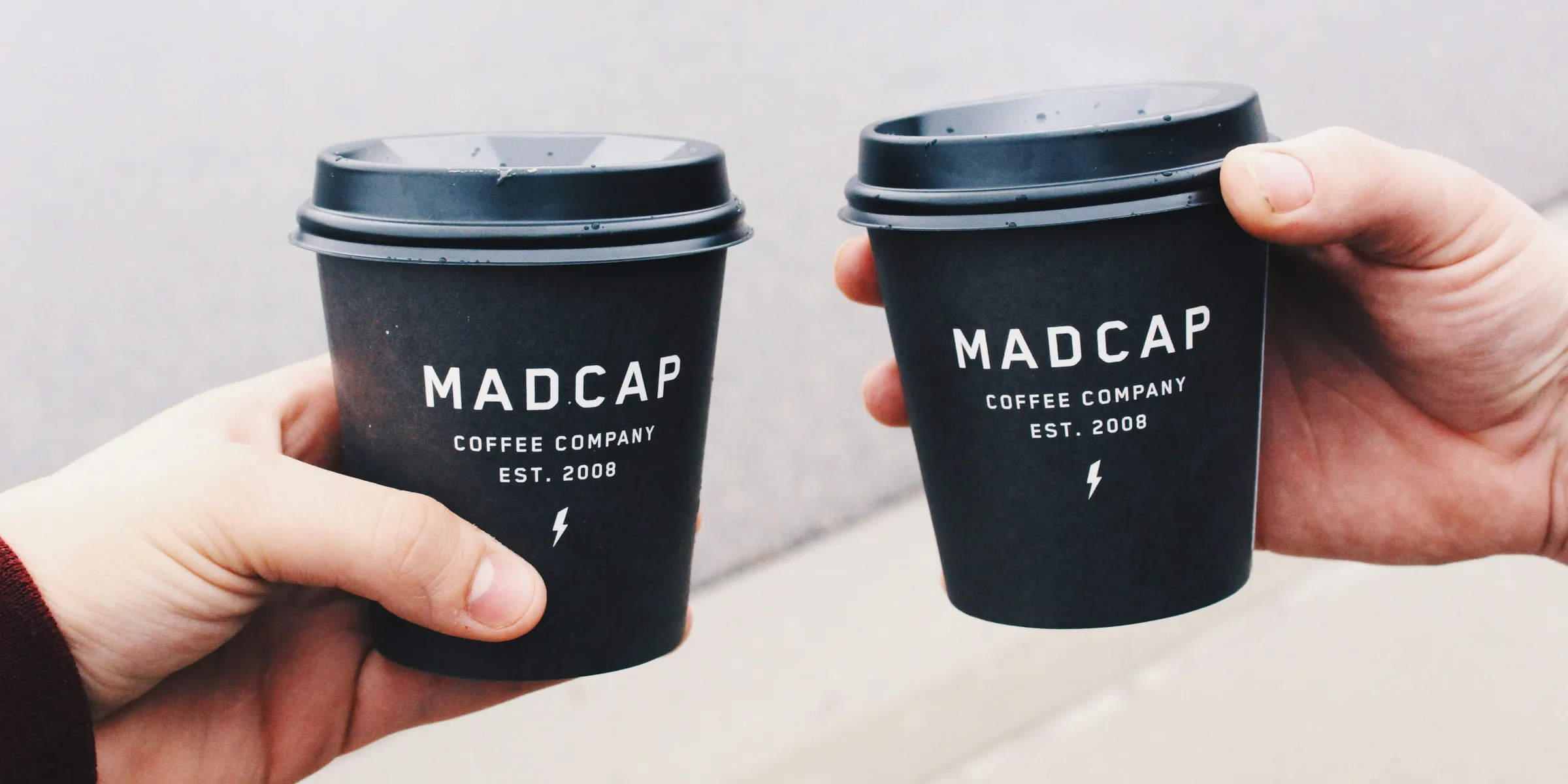 two person holding black Madcap coffee disposable cups