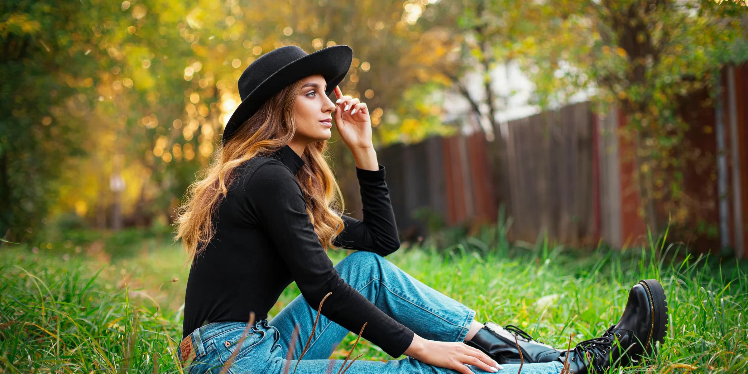 woman in black long sleeve shirt and blue denim jeans sitting on green grass during daytime