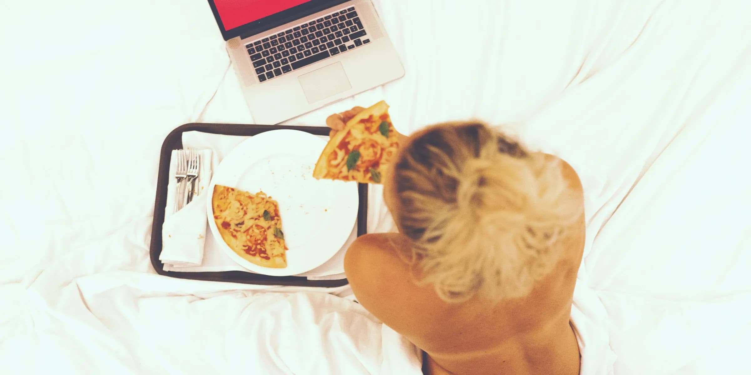 woman sitting on bed while eating pizza