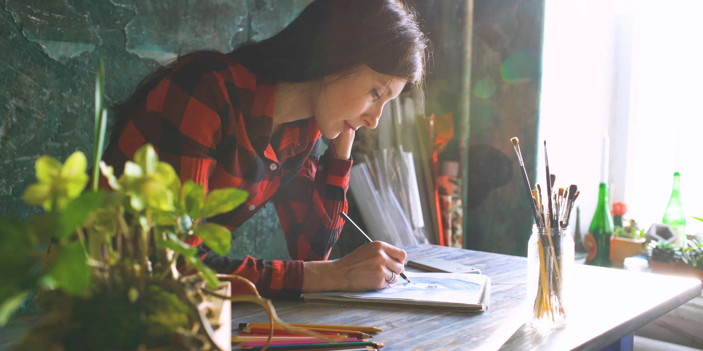 Young woman drawing at a desk with art supplies.