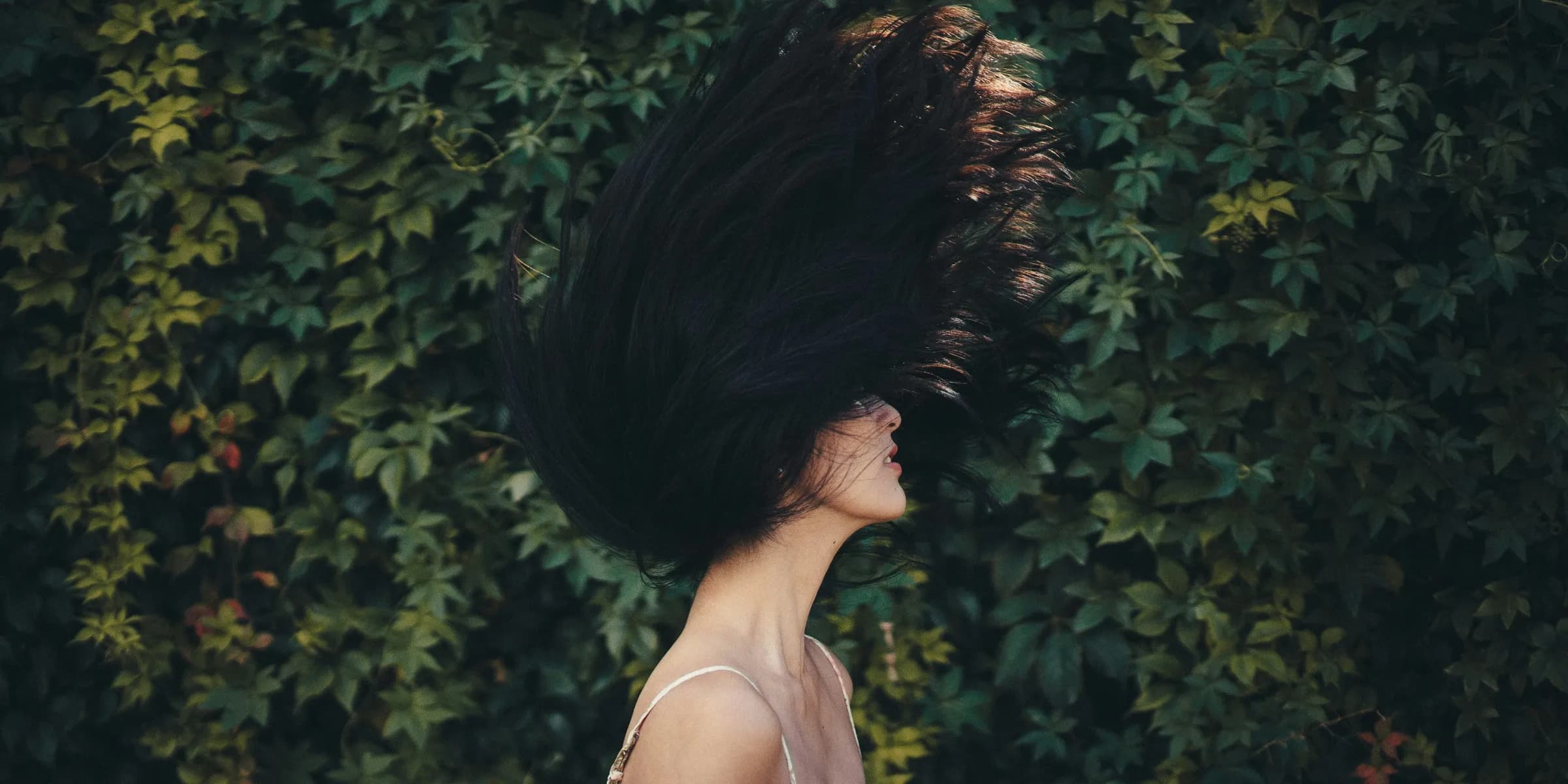 woman waving her hair in front of green leafed wall