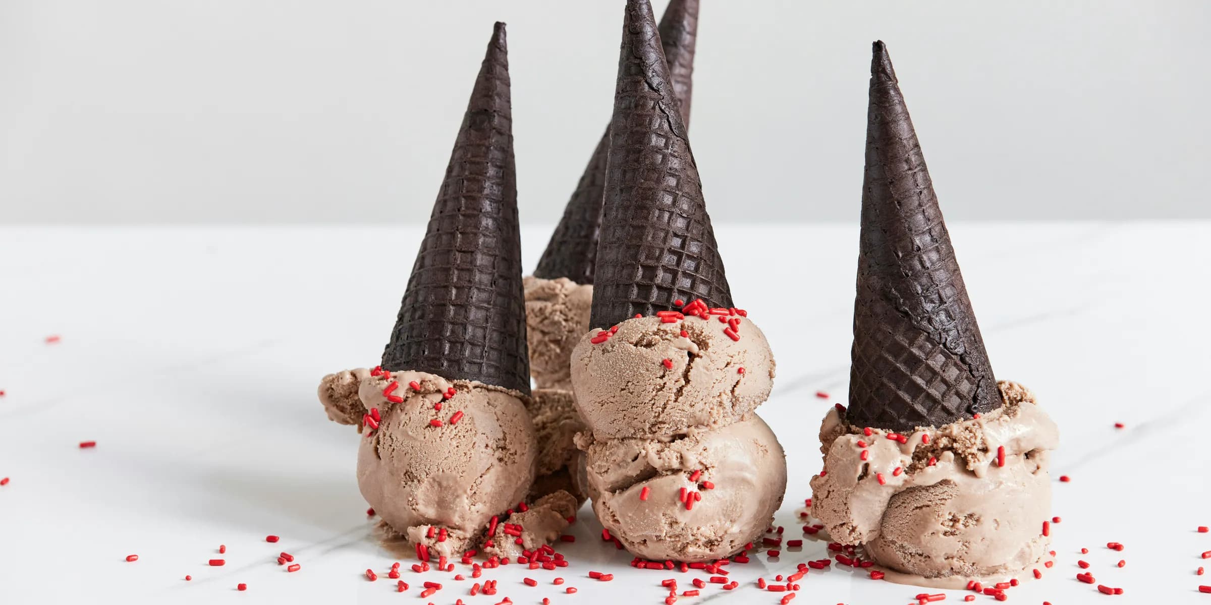 three cones of ice cream with sprinkles on a white surface