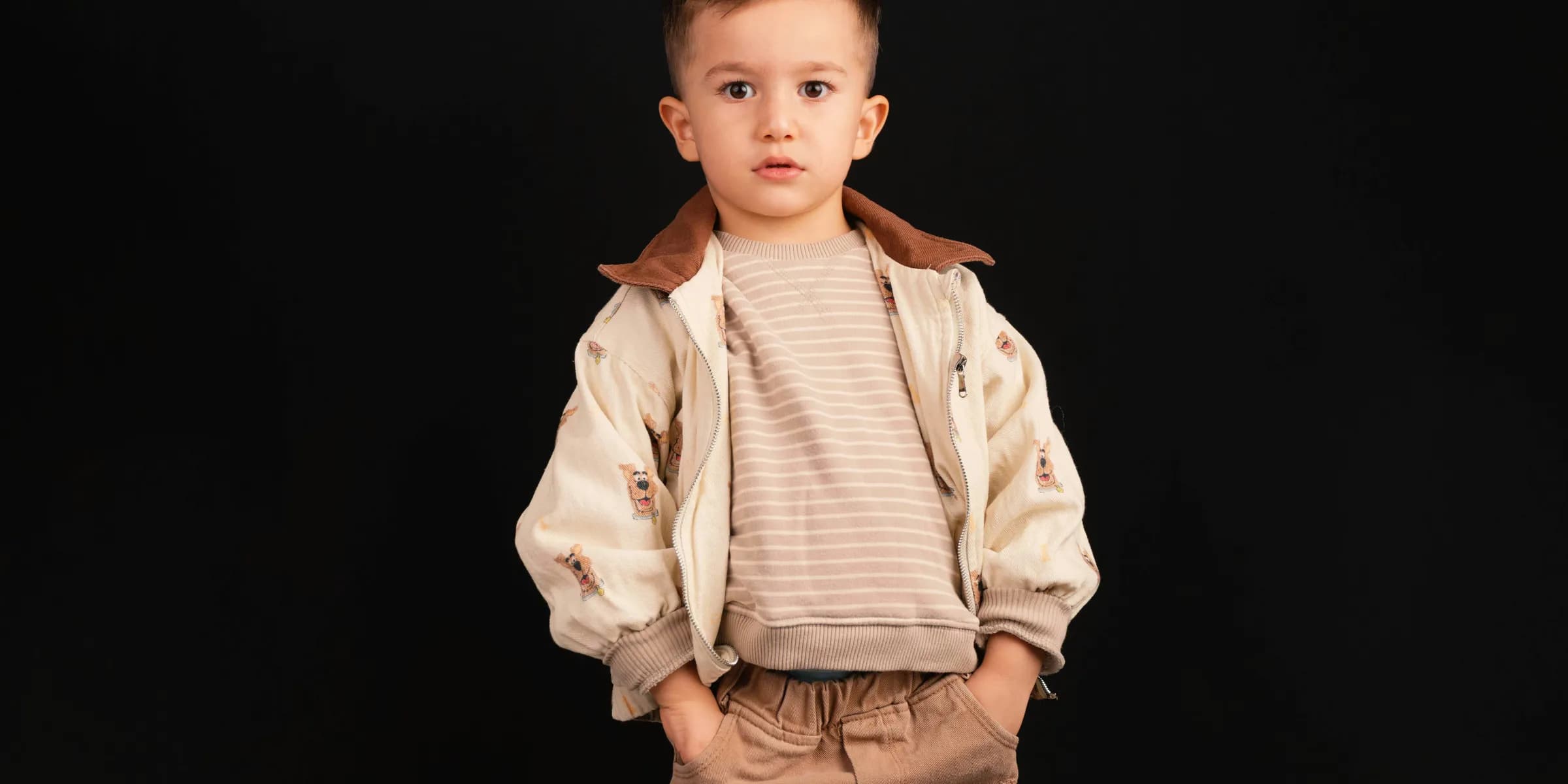 Young boy in stylish outfit stands against black background