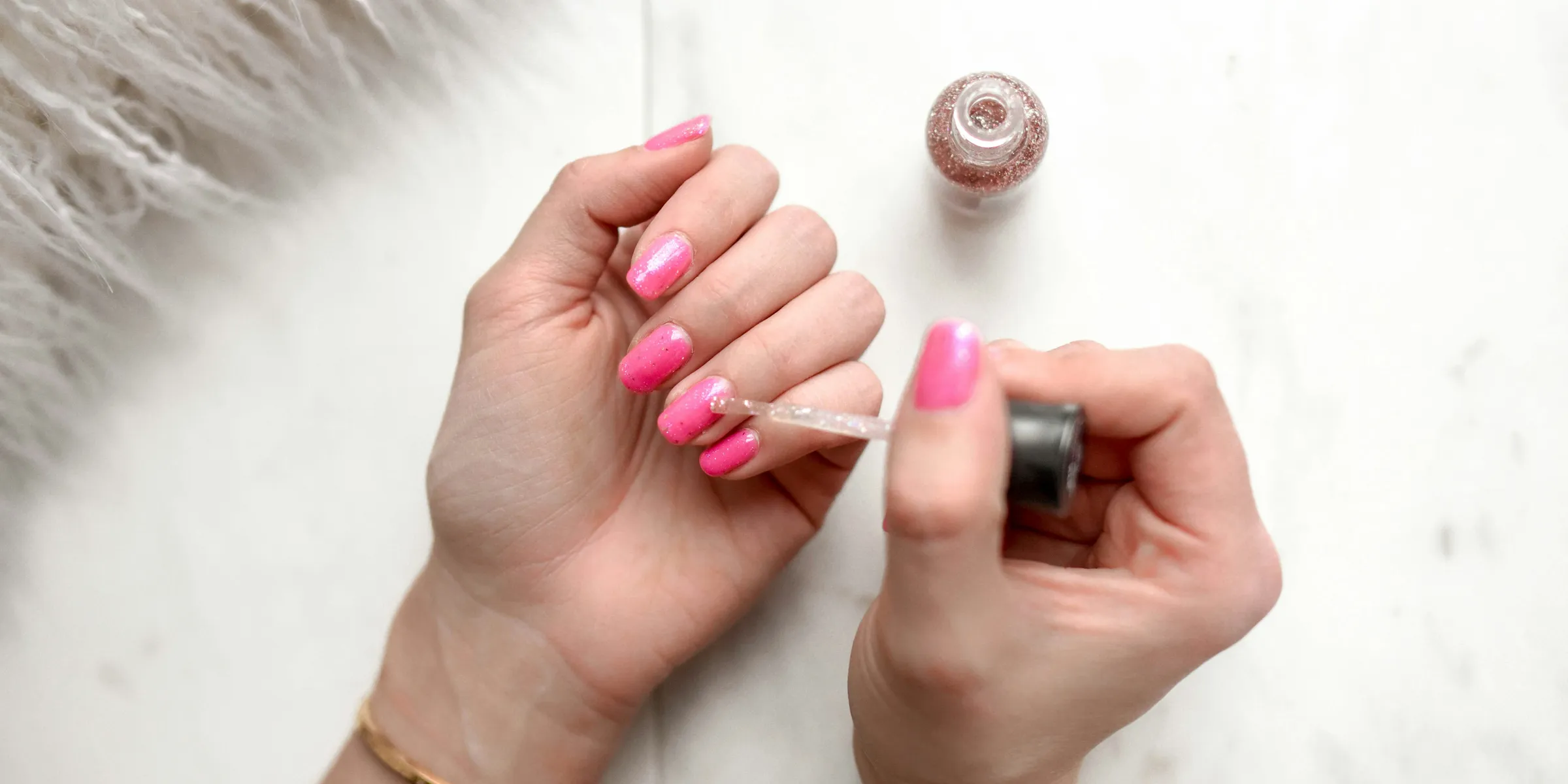 person spreading glittered nail polish on pink nails