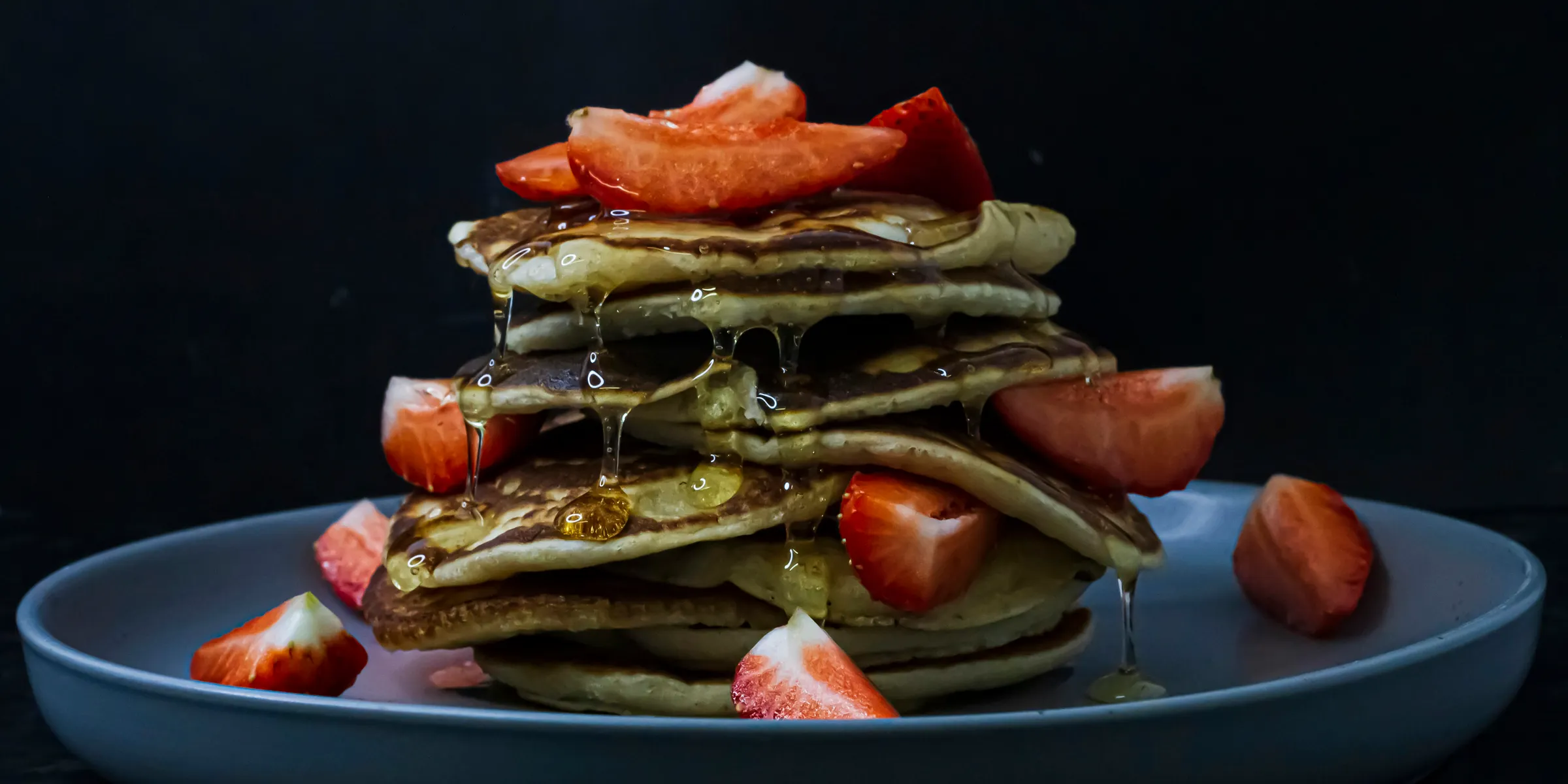 a stack of pancakes covered in syrup and sliced strawberries