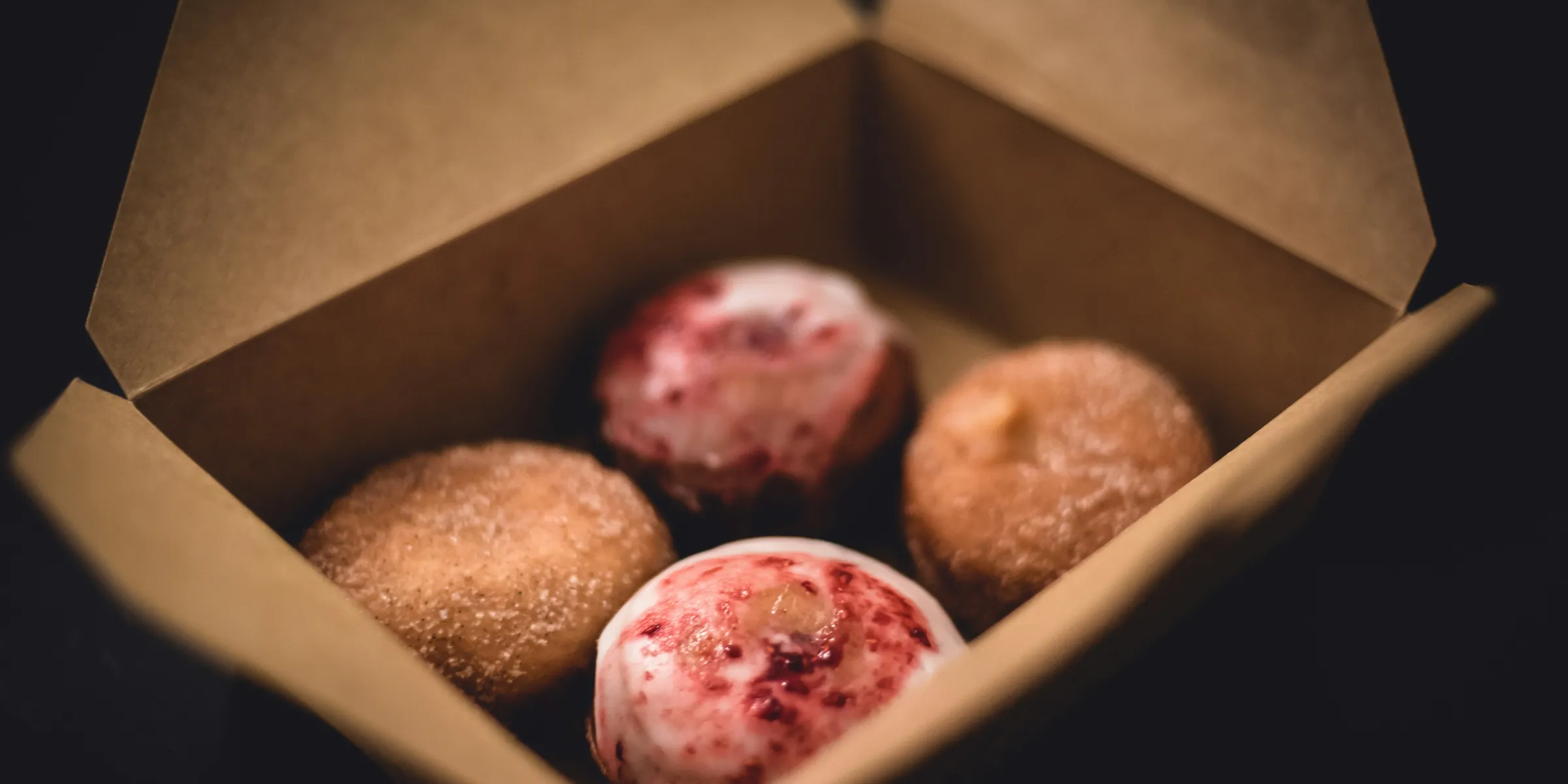 selective focus photography of four donuts in brown cardboard box