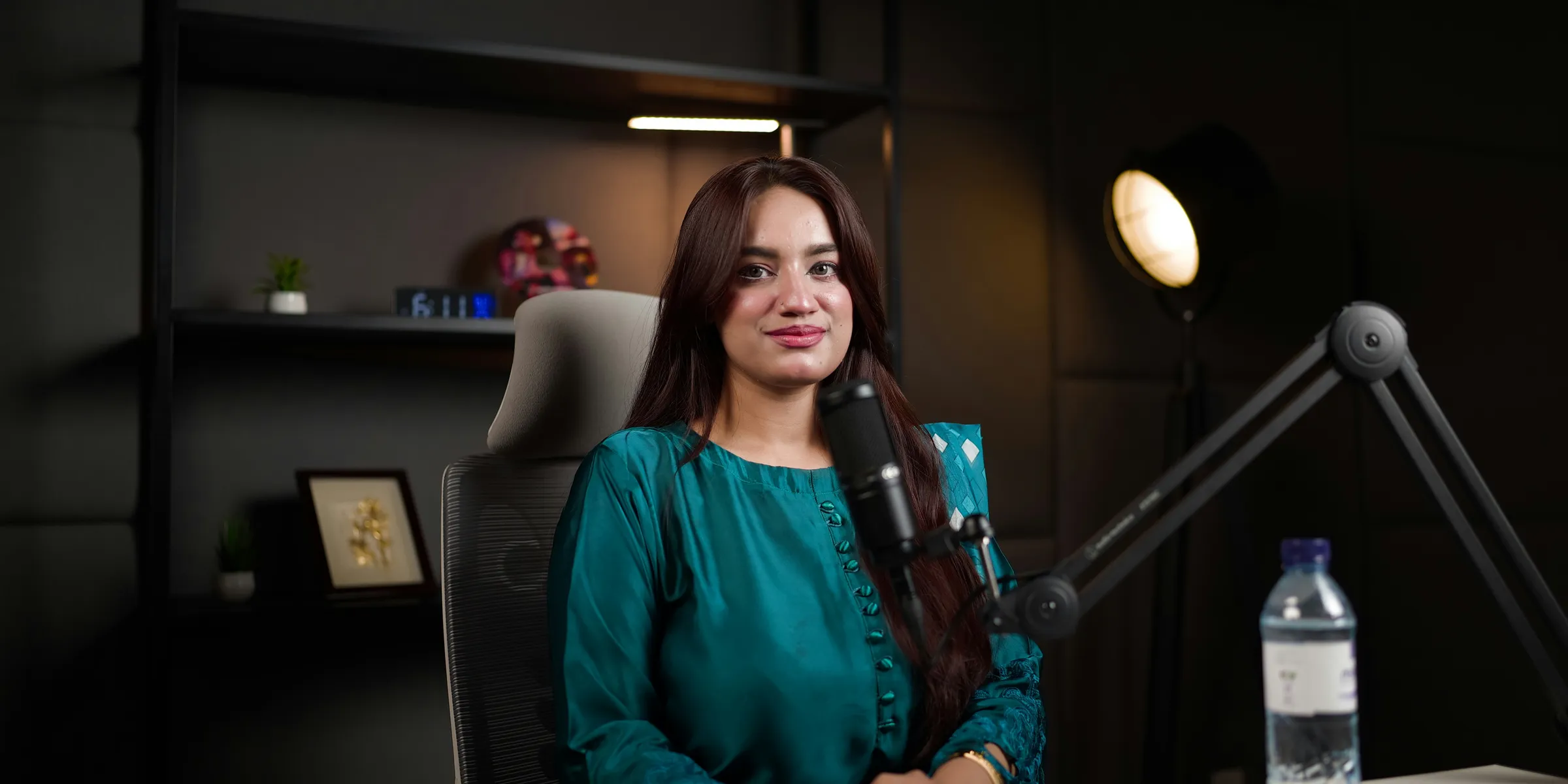 Woman sitting at desk with microphone and water bottle.