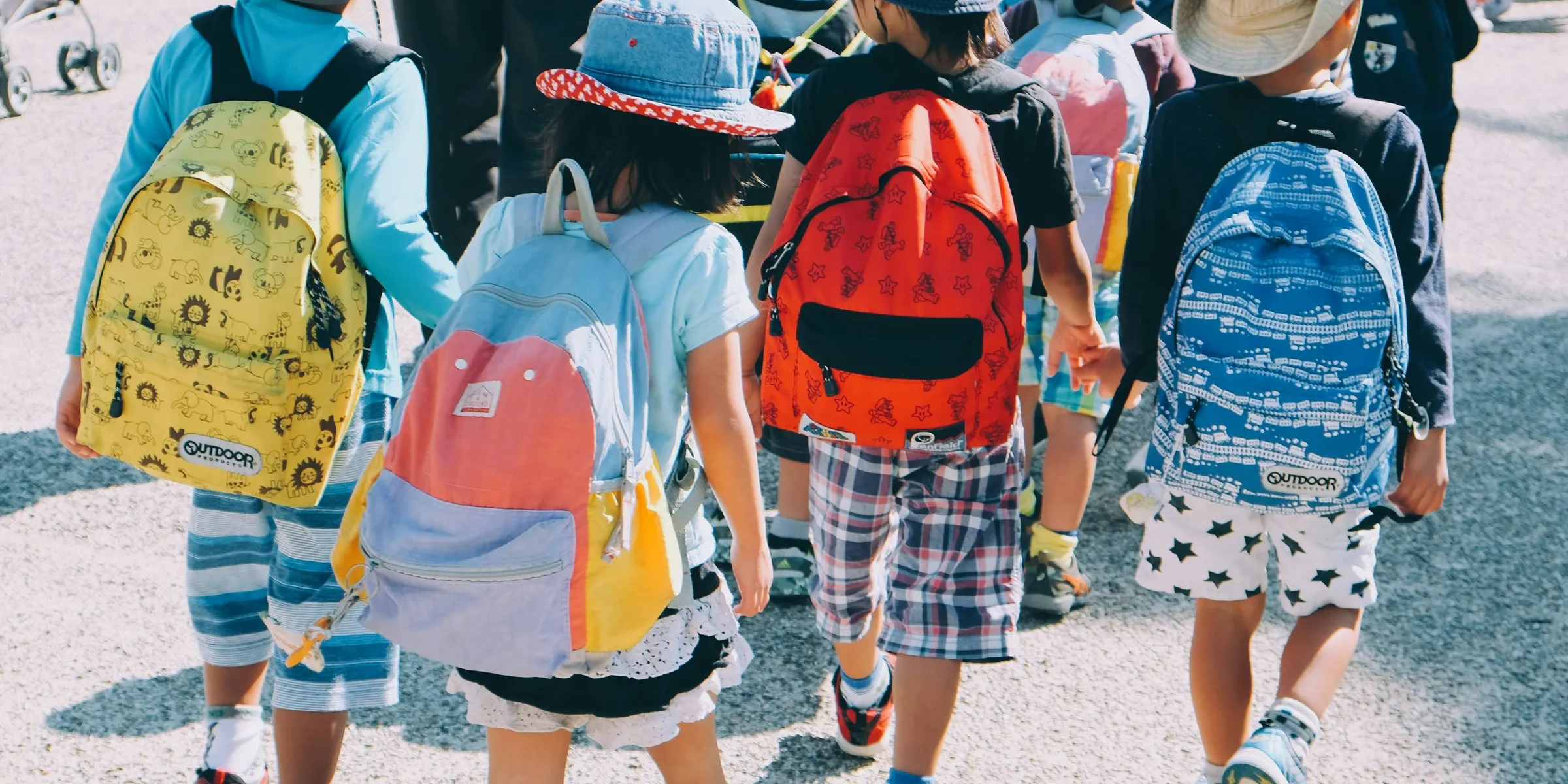 group of people wearing white and orange backpacks walking on gray concrete pavement during daytime