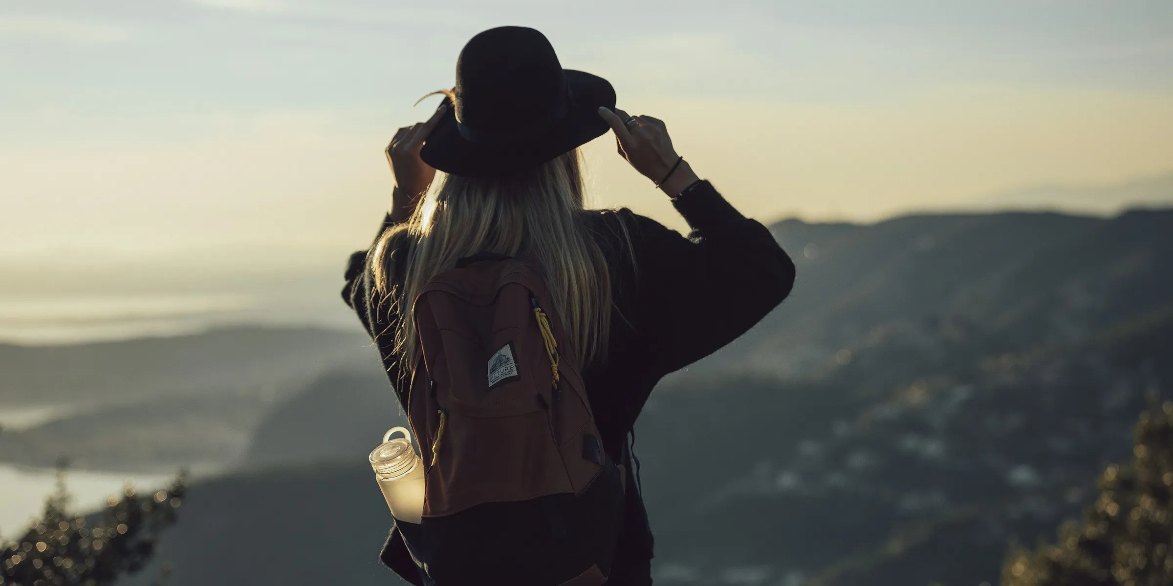 woman in gray hoodie and black pants wearing black hat standing on top of mountain during