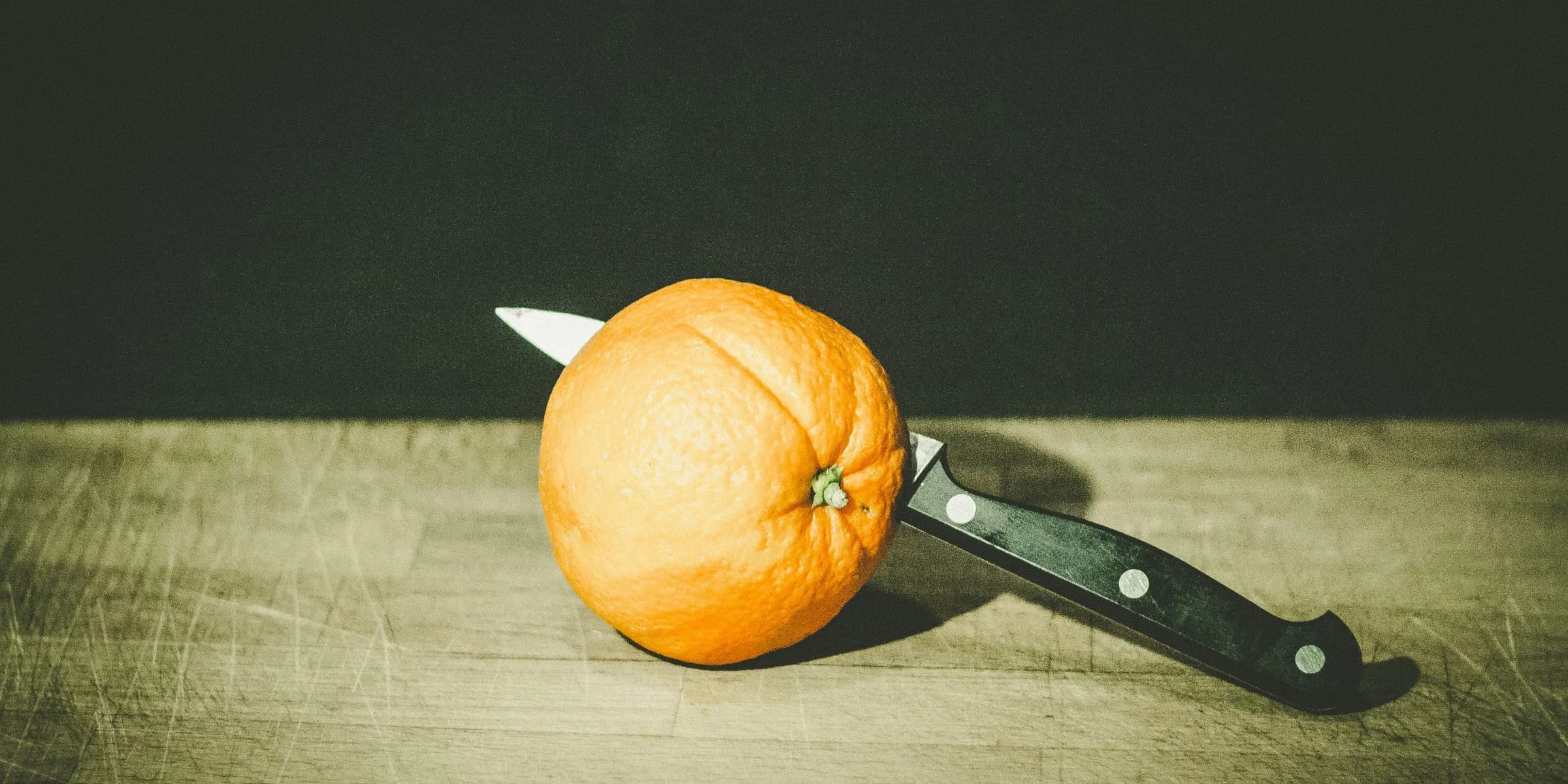 orange fruit and gray and black knife on brown wooden board low-light photography
