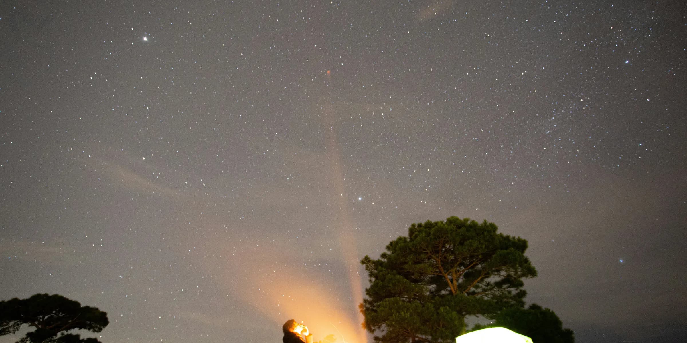 a couple of people sitting around a campfire under a night sky