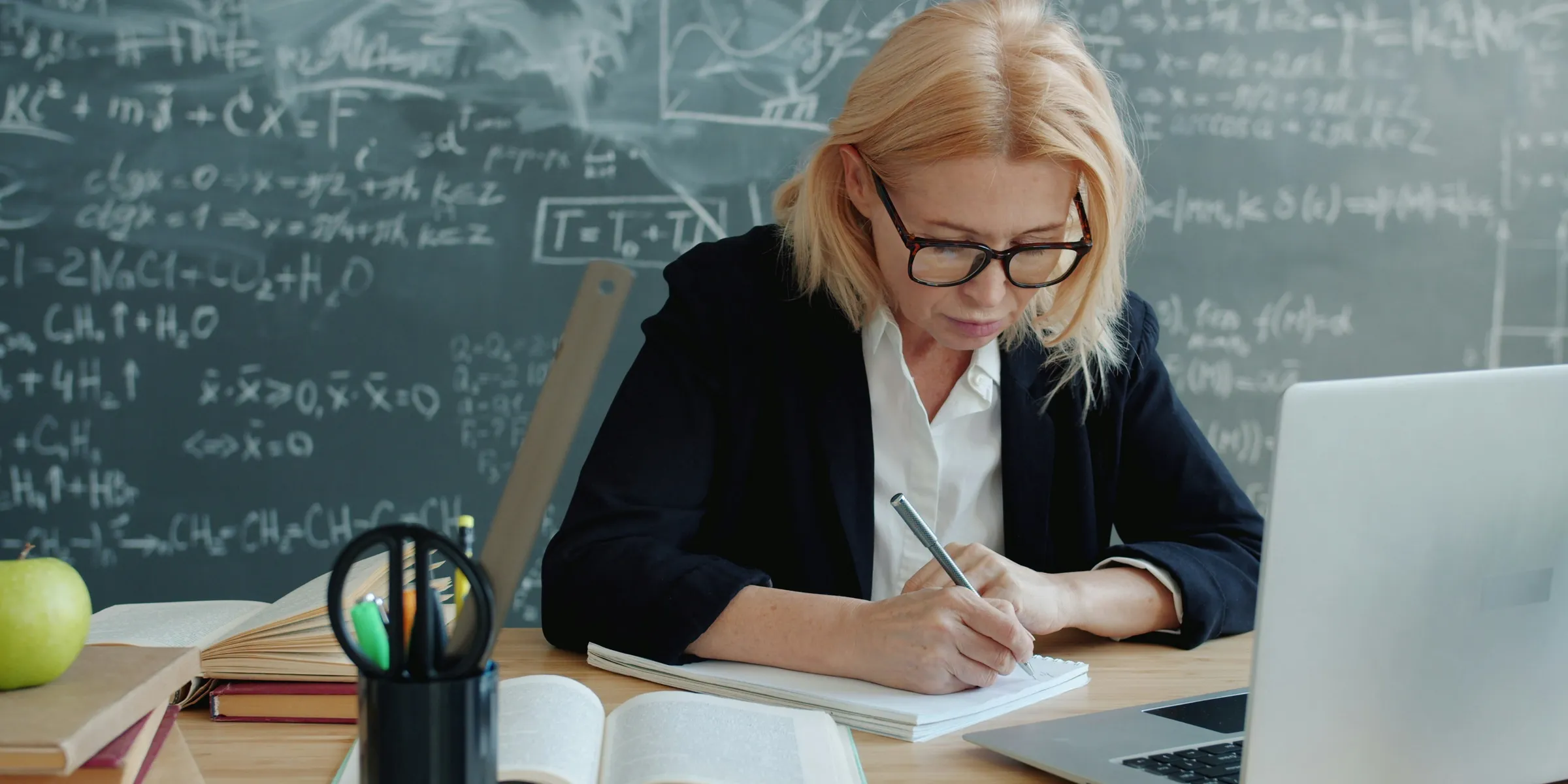 A woman writing in a notebook at a desk.