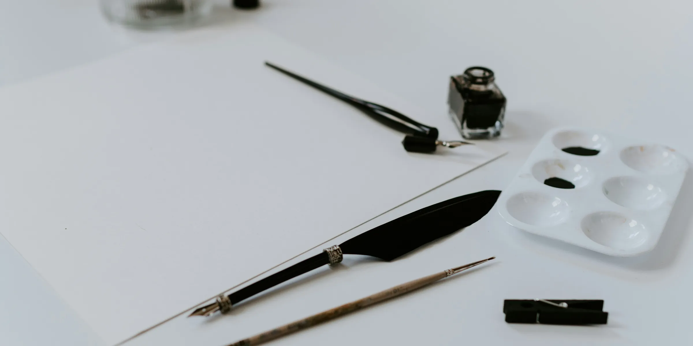 white paint palette with black paint beside ink bottle and paint brush